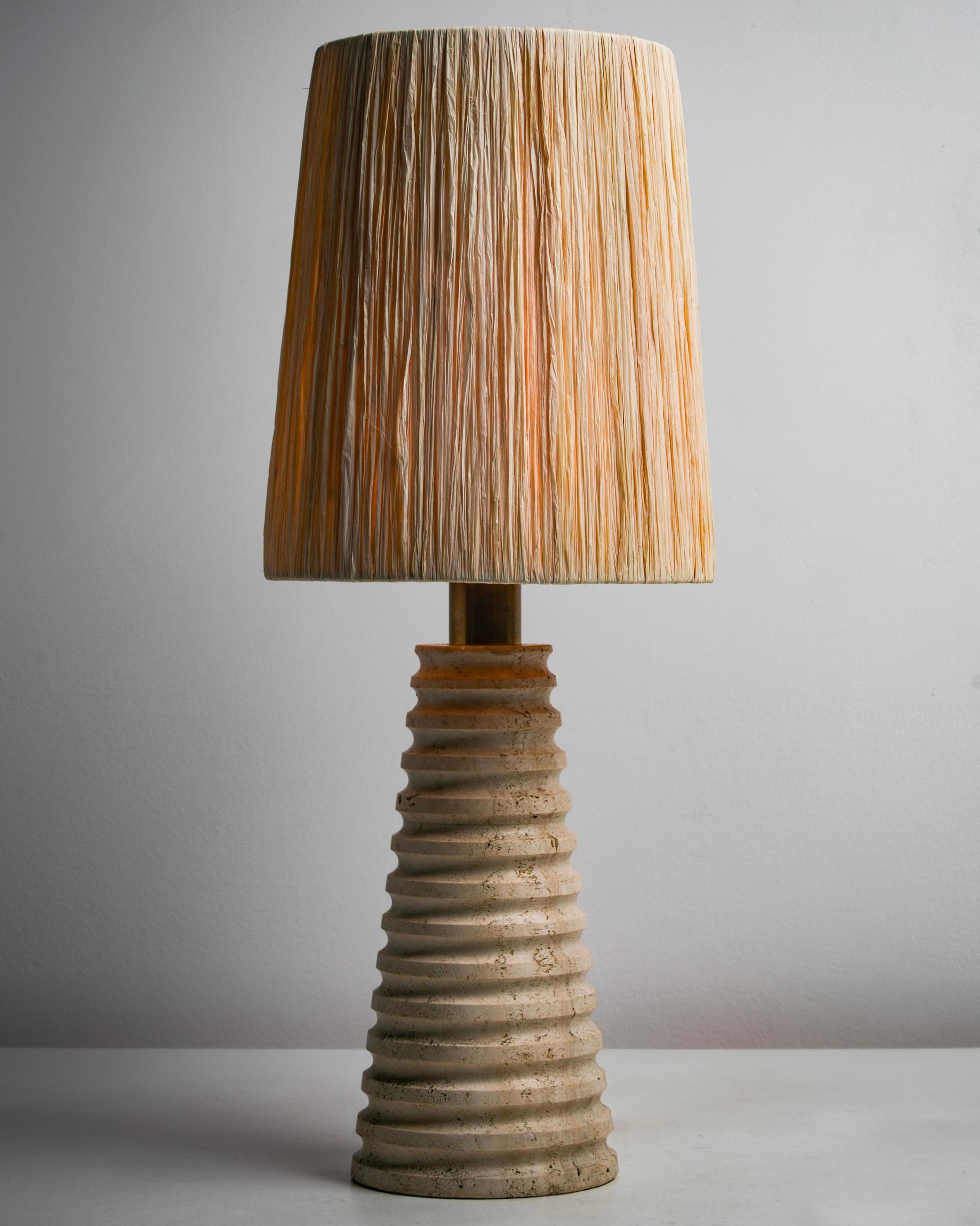 Italian carved travertine table lamp. Designed and manufactured in Italy, circa the 1970s. Tapered cylindrical base, carved in an upward spiral form. The shade is newly fabricated raffia. the lamp holds a single E27 socket type, adapted for the US.