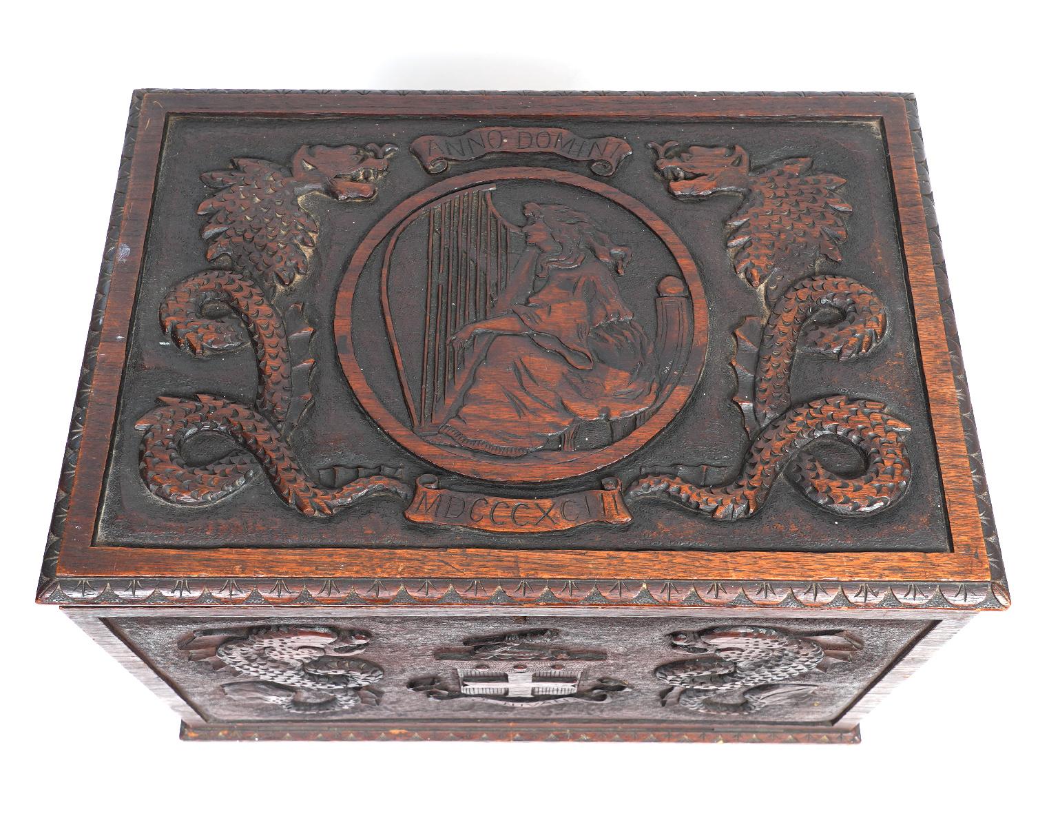 This rare Italian carved walnut captain's box or trunk features carvings on the top and three sides. The top shows an encircled domestic scene with a young woman playing the harp flanked by carvings of sea monsters and roman numerals dating it to