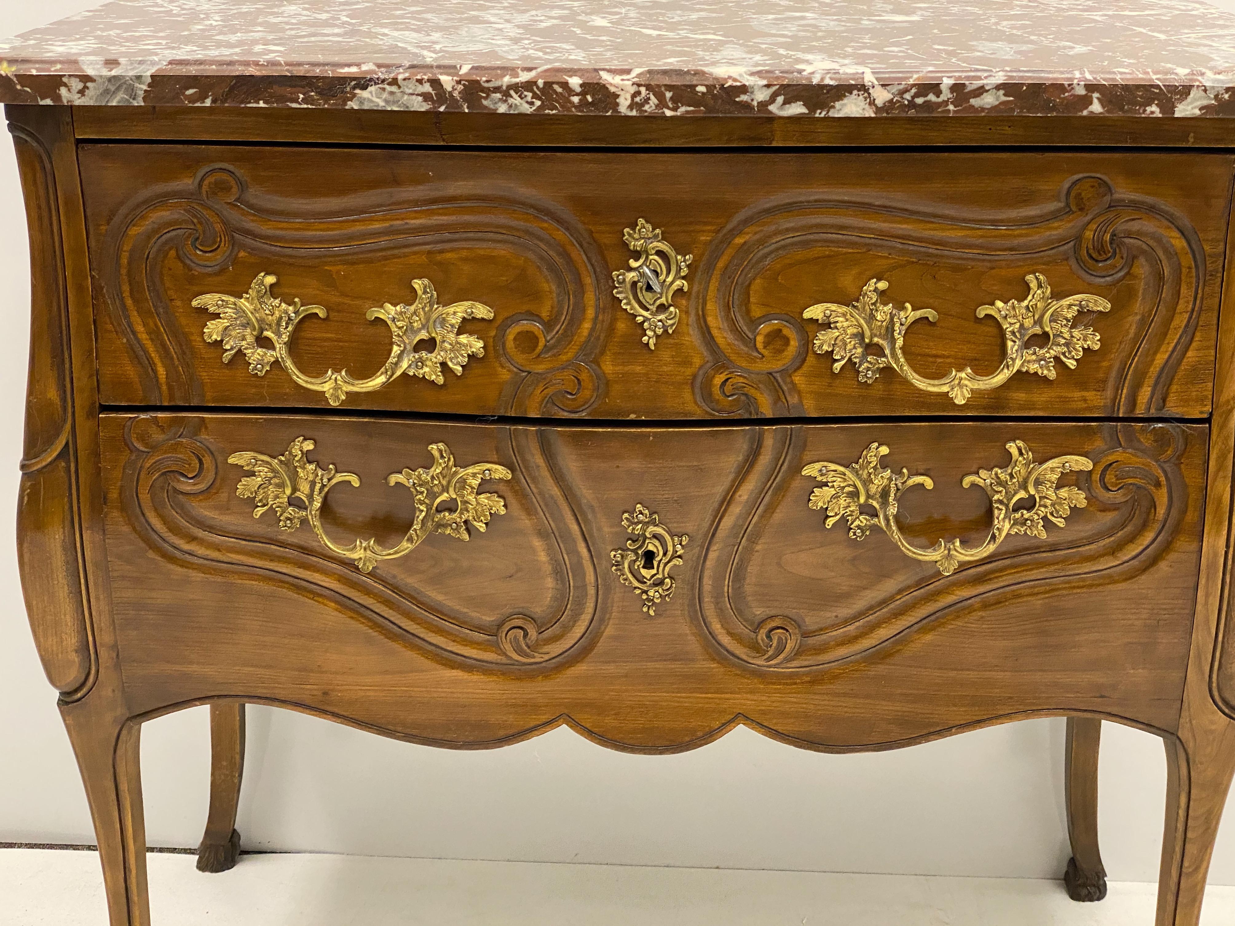 This is an Italian carved walnut chest with a rouge marble top. The piece has French styling, hairy paw feet, and the original hardware and key. It is unmarked. It most likely dates to the earlier part of the 20th century.