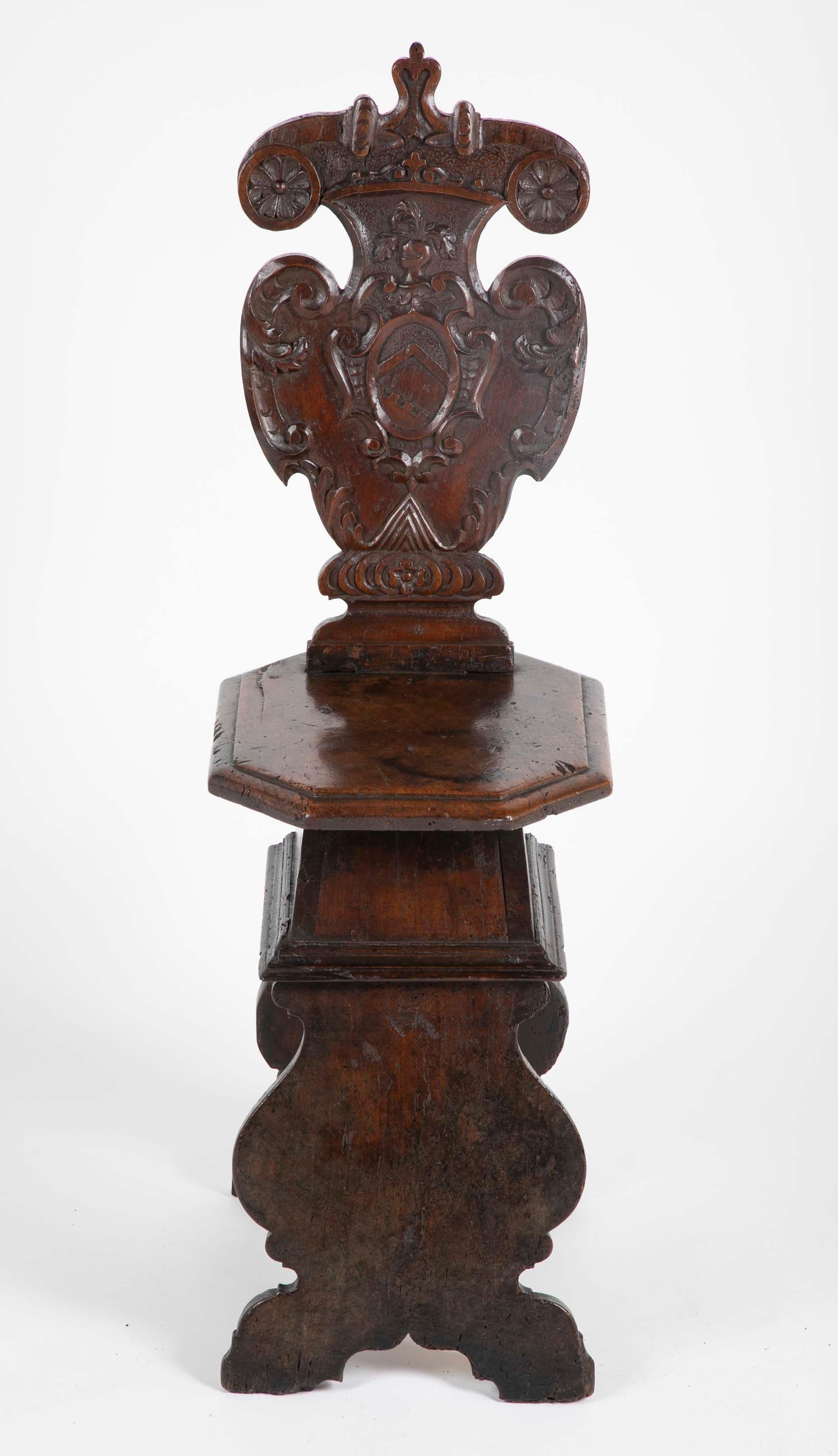 A late 16th, early 17th century walnut sgabello, or hall chair with a cartouche shaped back carved with a coats of arms armorial. The octagonal seat above scrolled supports. This is the classic late Renaissance, early Baroque form of a hall or