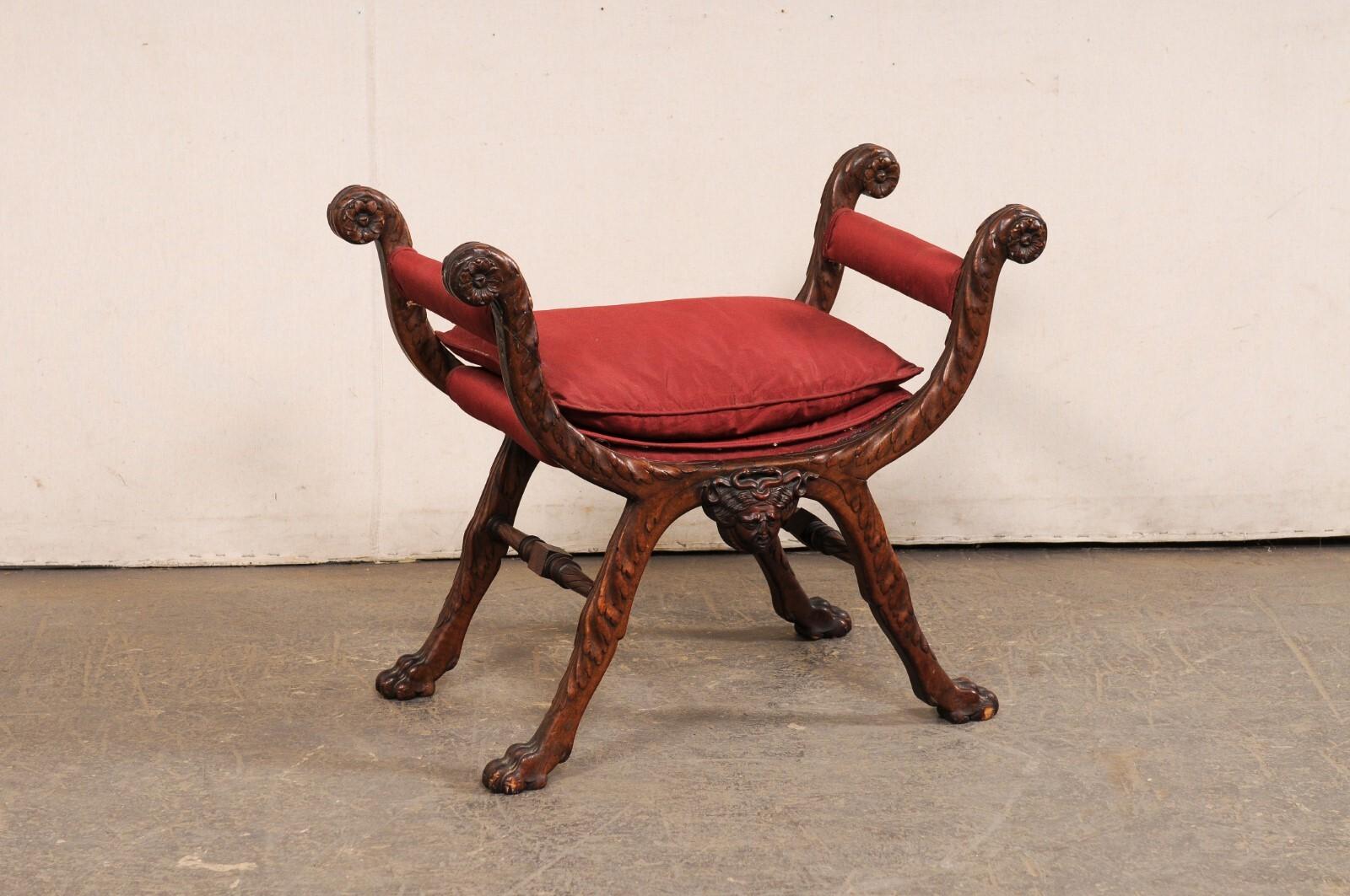 Taburete curul italiano de madera tallada con asiento acolchado de principios del siglo XX. Este taburete antiguo procedente de Italia ha sido creado en el estilo Curule (o a menudo llamado Dante), con patas compuestas por dos medias lunas, talladas