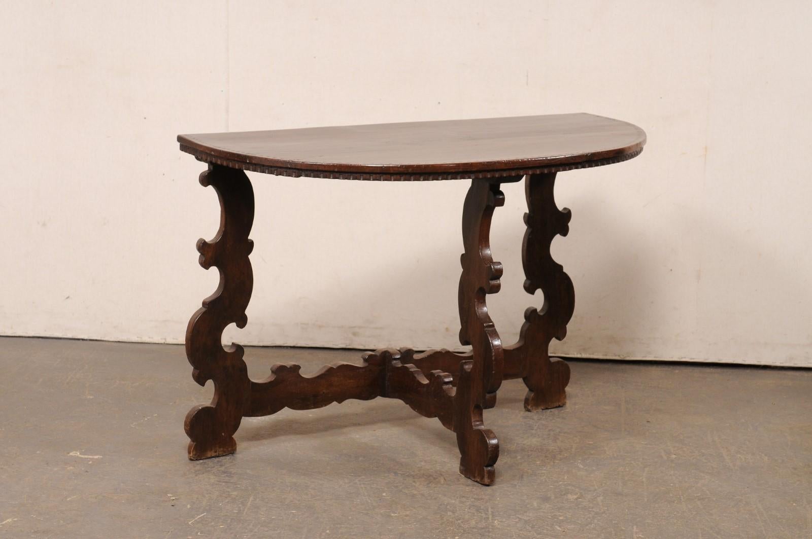 Console italienne en bois sculpté du XIXe siècle. Cette table ancienne d'Italie présente un plateau en forme de demi-lune, dont le dessous est orné d'une moulure en creux, au-dessus d'une base composée de trois pieds et d'une entretoise en forme de