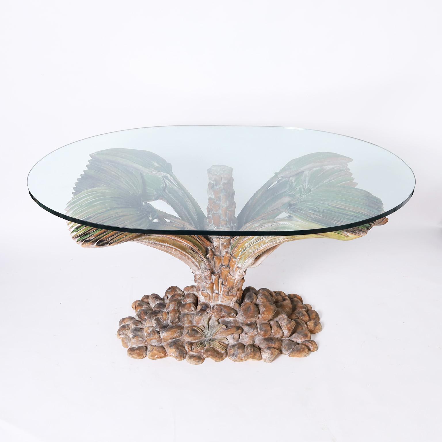 Impressive mid-century Italian dining table with an oval glass top supported by a carved and painted walnut palm plant having multiple leaves and a trunk in a faux rock pile base. Increasing the size of the glass top will allow for a larger dining