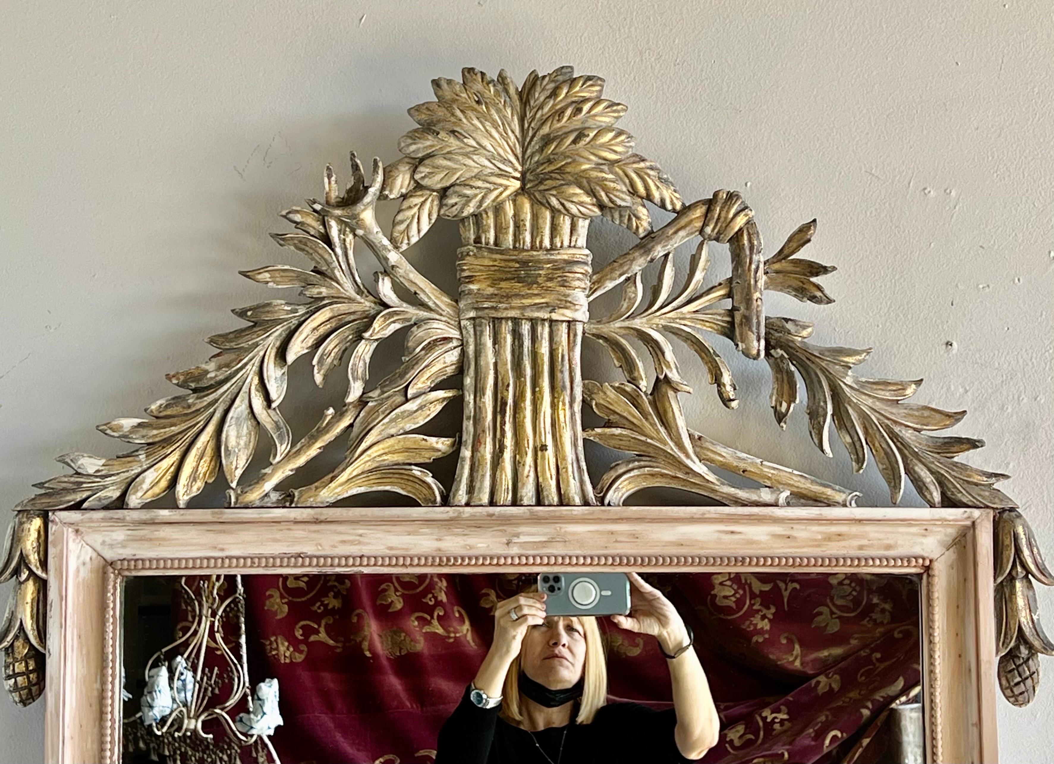 Italian carved wood mirror with gold leaf details. The top of the mirror is adorned with bunches of wheat. There is also leaves flanking the wheat. The finish is beautifully distressed with accents of gold leaf throughout.