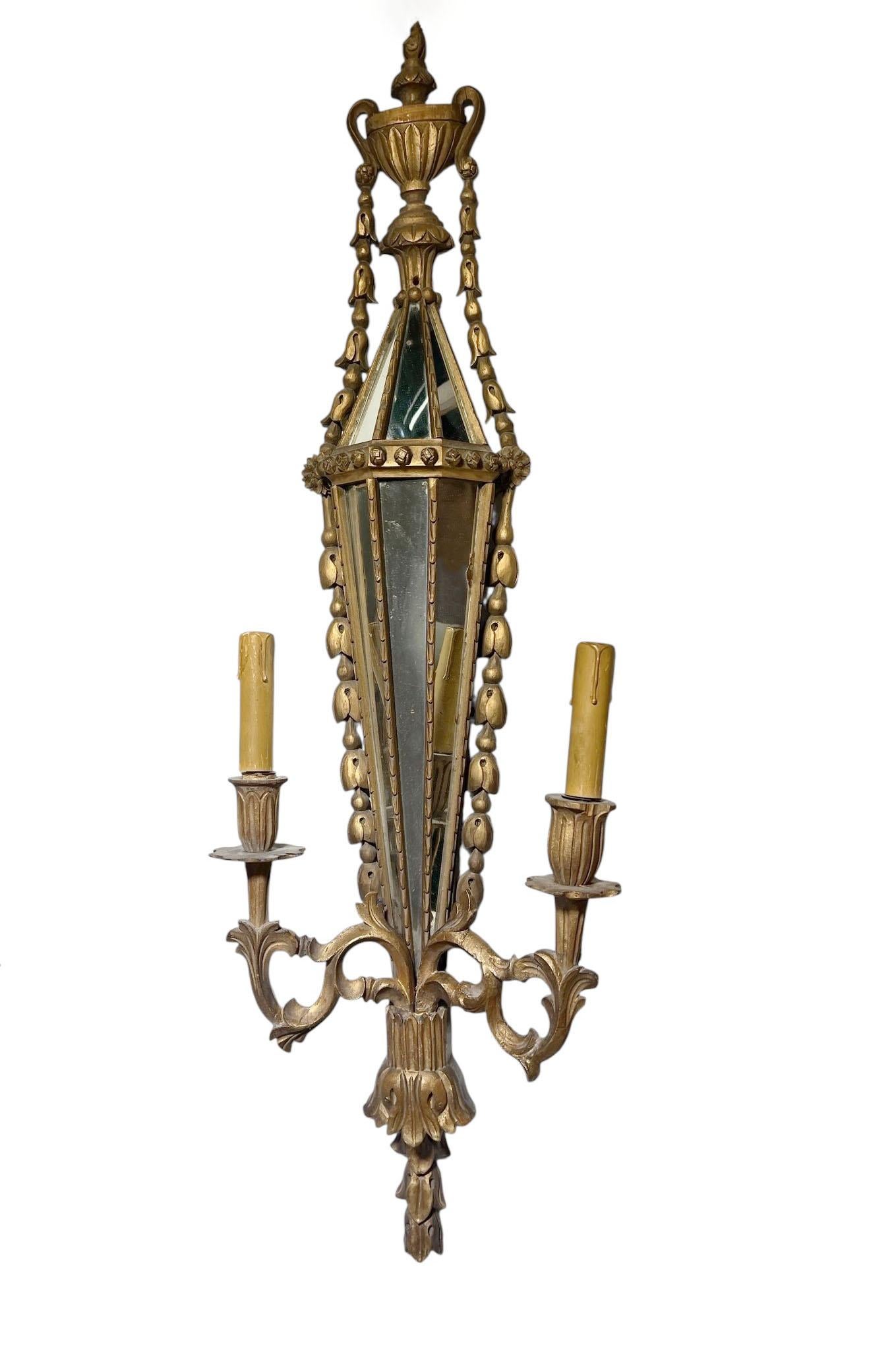 A striking pair of Italian carved wood sconces with inlaid mirrors, circa 1890s. Each sconce features an elegant elongated form, beautifully hand carved with scrollwork and foliate detailing, accentuated by inset mirror panels that reflect light and