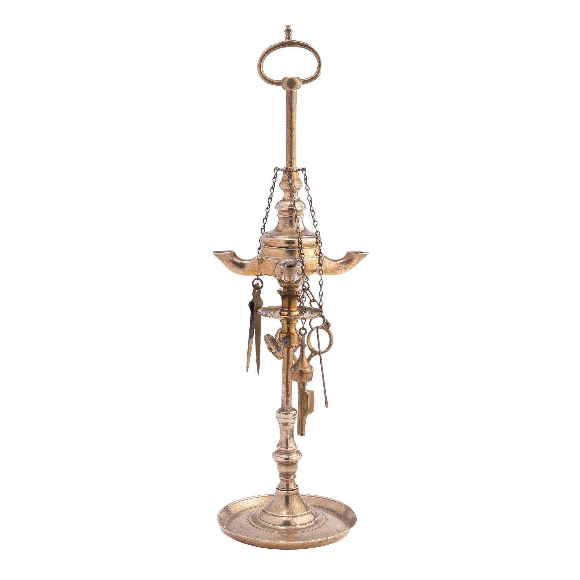 Cast brass four burner Lucerne oil lamp with four hanging wick tools, an adjustable under-font collection dish, and a loop carrying handle at the top of the rod.

Italy, circa 1810.