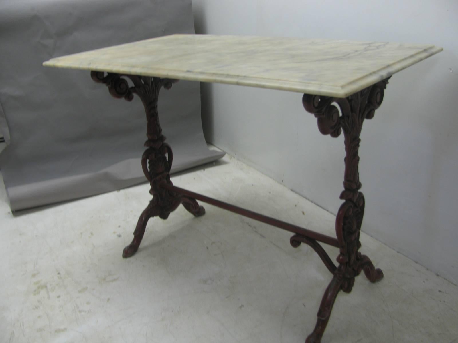 Finely detailed cast iron base with a Carrara marble top. Base still has its original red paint while the marble has endured its life collecting some discoloration. Marble top has a little nick on the underside of one edge (pictured). Both the