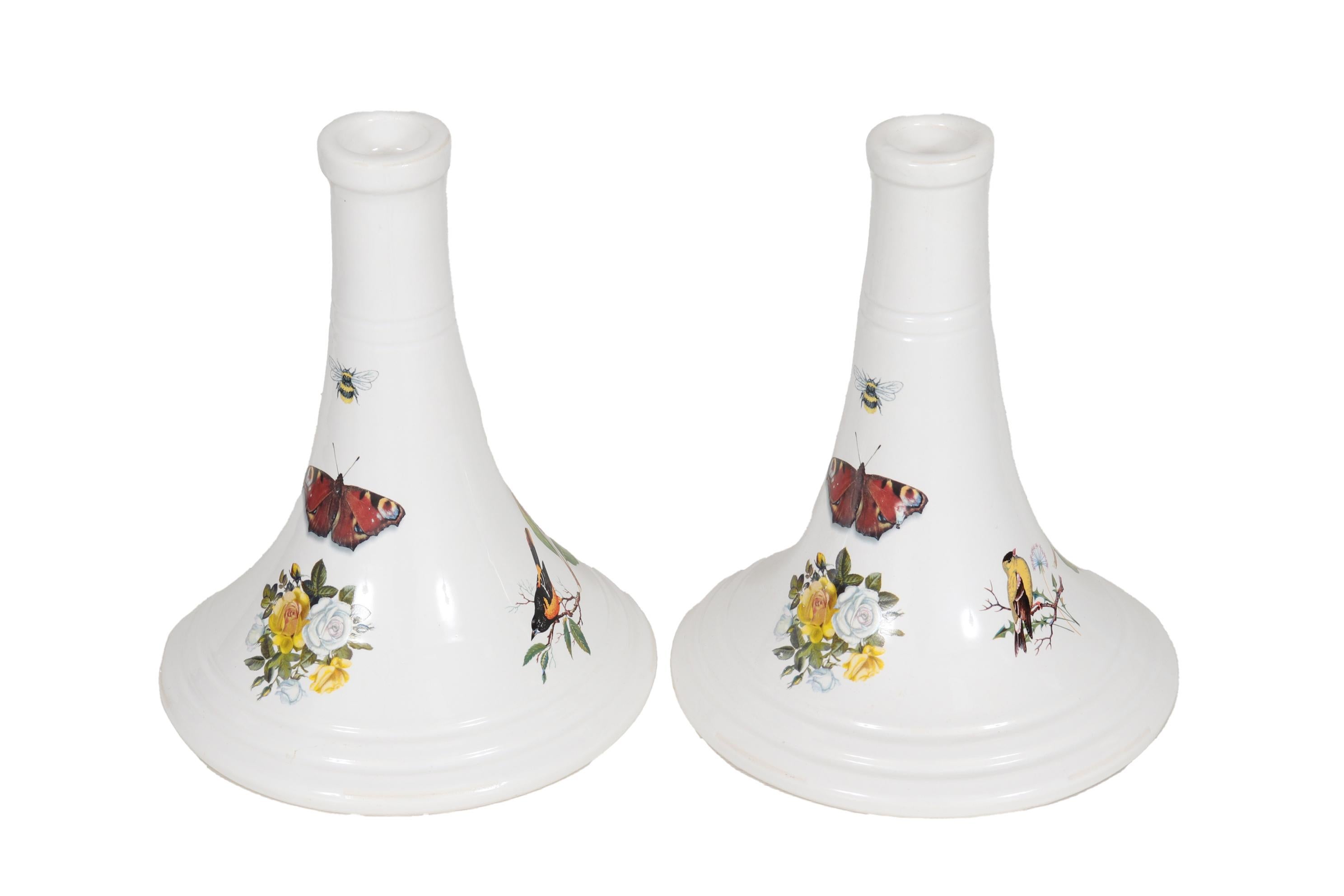 A pair of Italian ceramic candlestick holders. White conical shaped holders are decorated with transferware patterns including white and yellow roses and honeysuckle, orange and yellow orioles, monarch butterflies and bees. Dimensions per candle