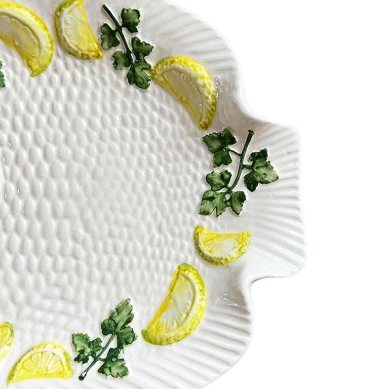 A small ceramic Italian fish serving plate by Bassano. Glazed in a creamy white, and in the shape of a fish, this dish will be perfect for a table setting, or as a catchall. It is decorated with textured scales and a fin, and yellow-green trompe