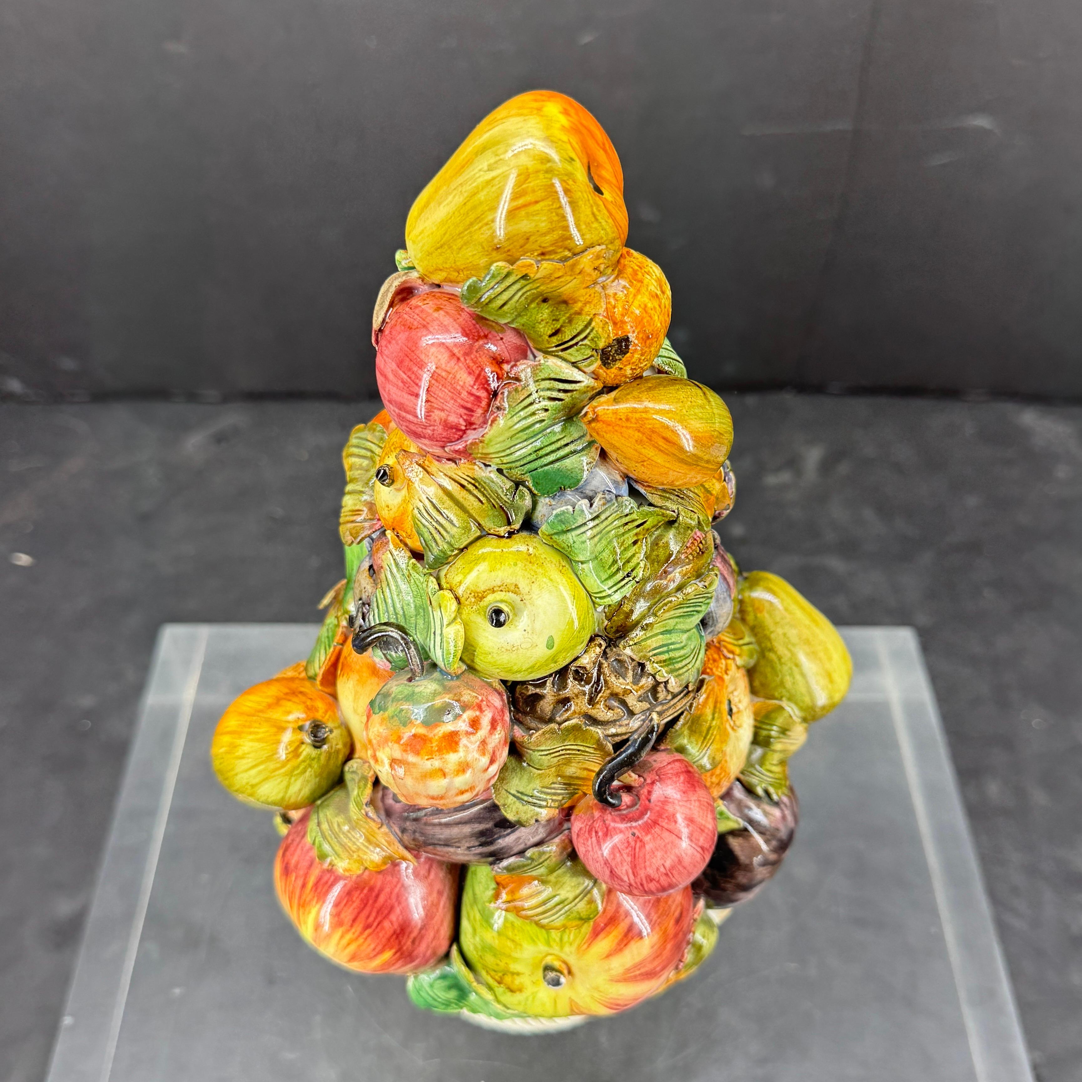 Escultura figura de cesta de fruta de cerámica esmaltada italiana. Esta compota está hecha a mano con la mayor atención al detalle. Vemos esta pieza en una encimera o mesa de cocina. La cesta lleva la marca IITALY en la base.
