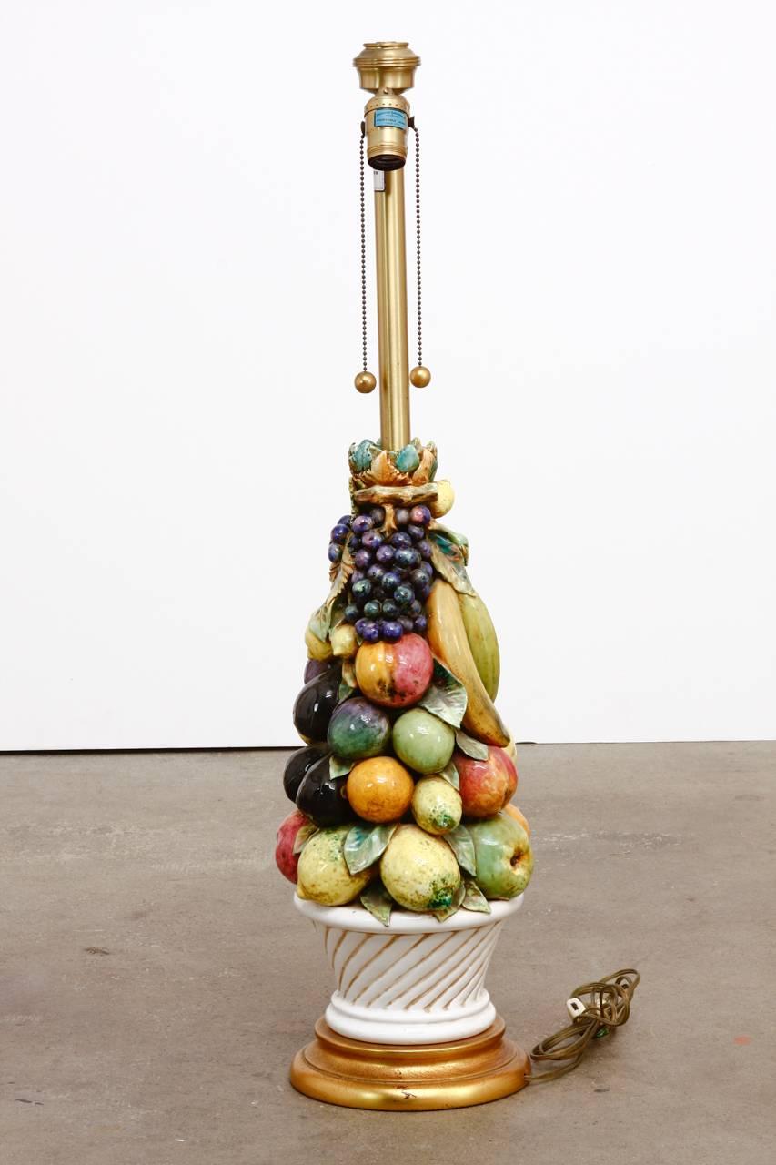Beautiful Italian ceramic fruit topiary table lamp produced by Marbro Lamp Co. Features a colorful cornucopia of mixed fruit in a white basket. The lamp has a giltwood stepped base and is topped with a brass column holding double head hardware. The