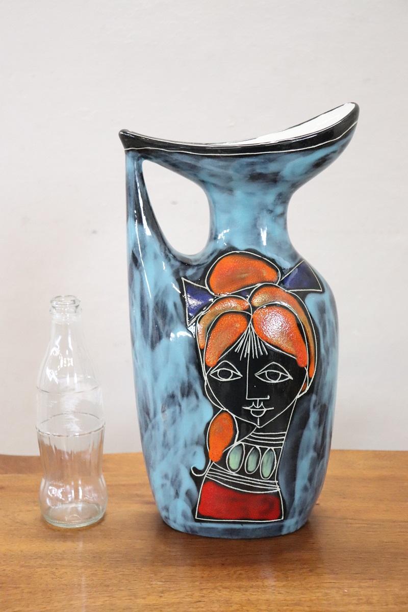 We present this beautiful Italian carafe vase (circa 1960s) with a particular futuristic design.

The vase is made of ceramic with enamel decoration in the main shades of blue. On both sides there is an abstract face of a cheeky girl with flashy
