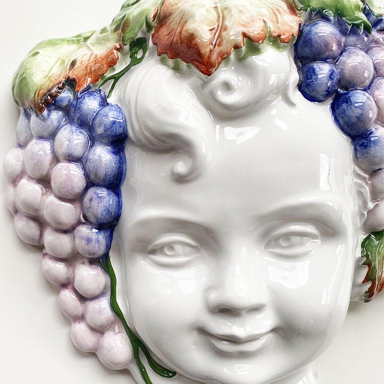 A unique whimsical ceramic majolica wall hanging of the infant Bacchus. Any lover of wine will love this fabulous wall hanging. The piece depicts the god of winemaking in crisp white glazed ceramic. His head is decorated in an ode to his other