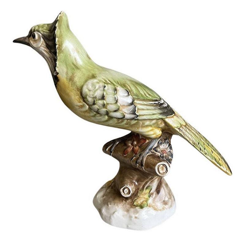 A hand-painted ceramic bird figurine in green and yellow. Unfortunately, we are not bird experts, but we think it may be a Jaybird or something similar. It is hand-painted in green, with a yellow breast. He has a black beak and stands upon a brown