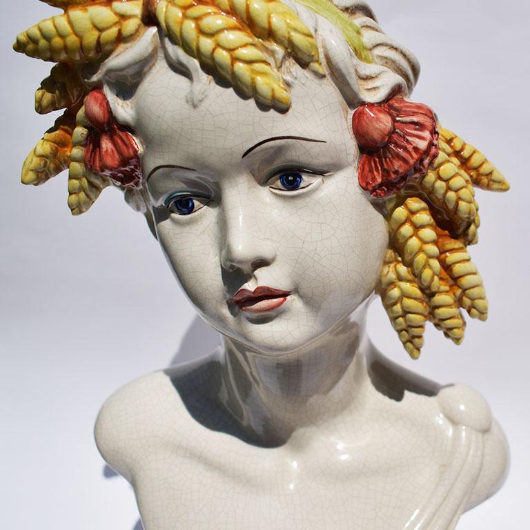 Beautiful rare ceramic hand painted bust. A lovely accent piece for any room. This figure features a woman with a crown of yellow wheat and blue and white tassels atop her head. Her hair is swept up and she wears a draped gown. In an antique white