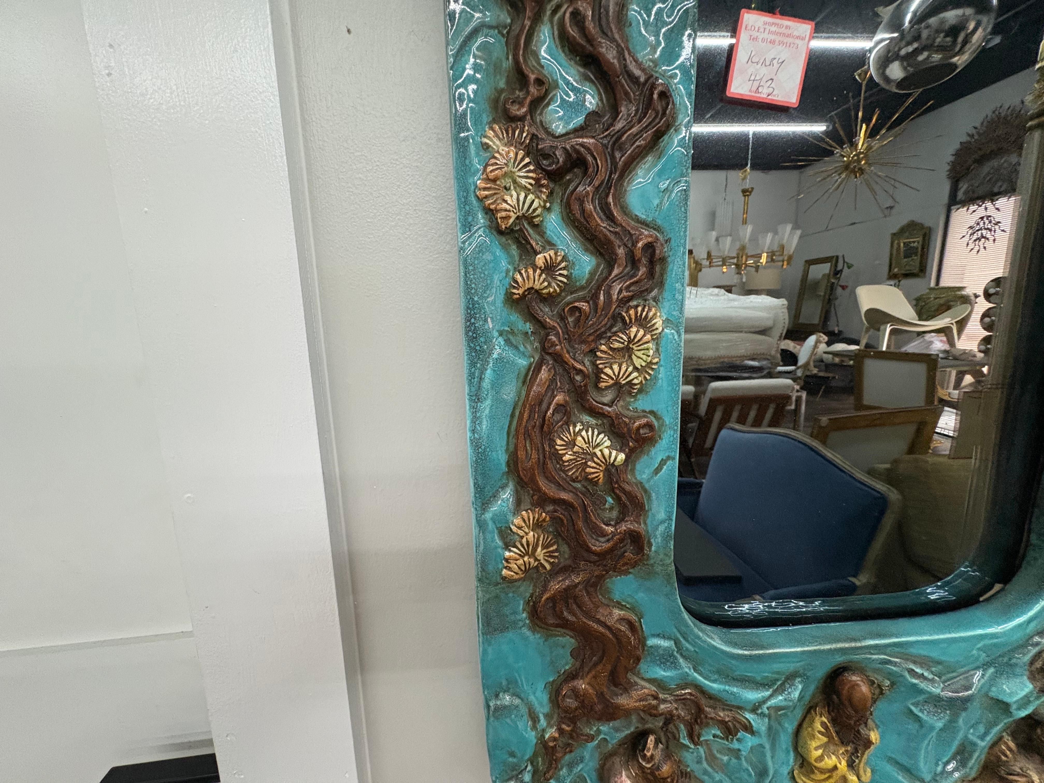 Italian Ceramic Mirror. 
Offered is a beautifully detailed Italian Hollywood Regency mirror from the 1960's. This shapely Italian mirror in a lovely shade of blue features three Asian figures and three monkey figures surrounded by a well detailed