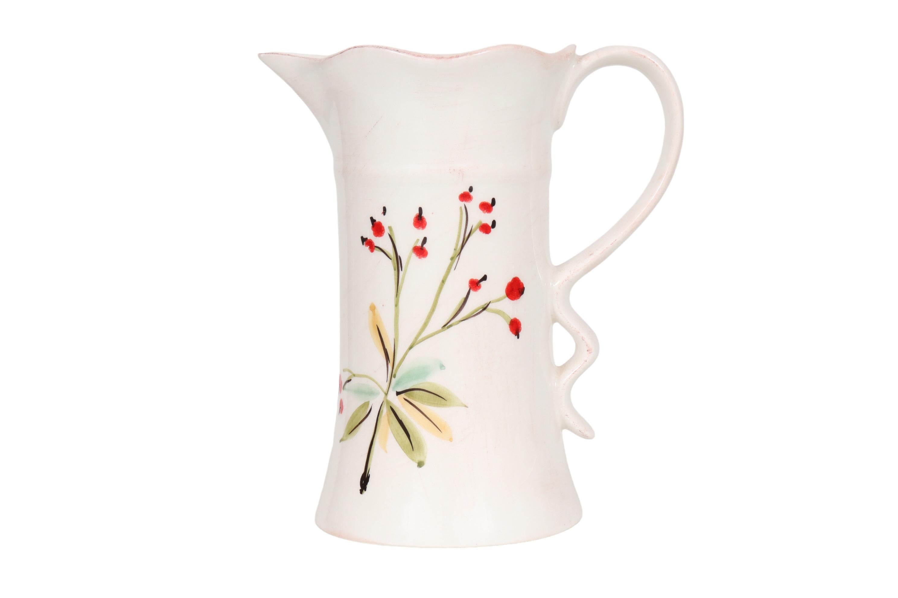 An Italian ceramic pitcher made by Tiriduzzi. Hand painted with a simple floral spray of red poppies on a white background. The lip is lightly ruffled, this wave mirrored in the base of the loop handle. Marked underneath “Ceramiche Umbre by