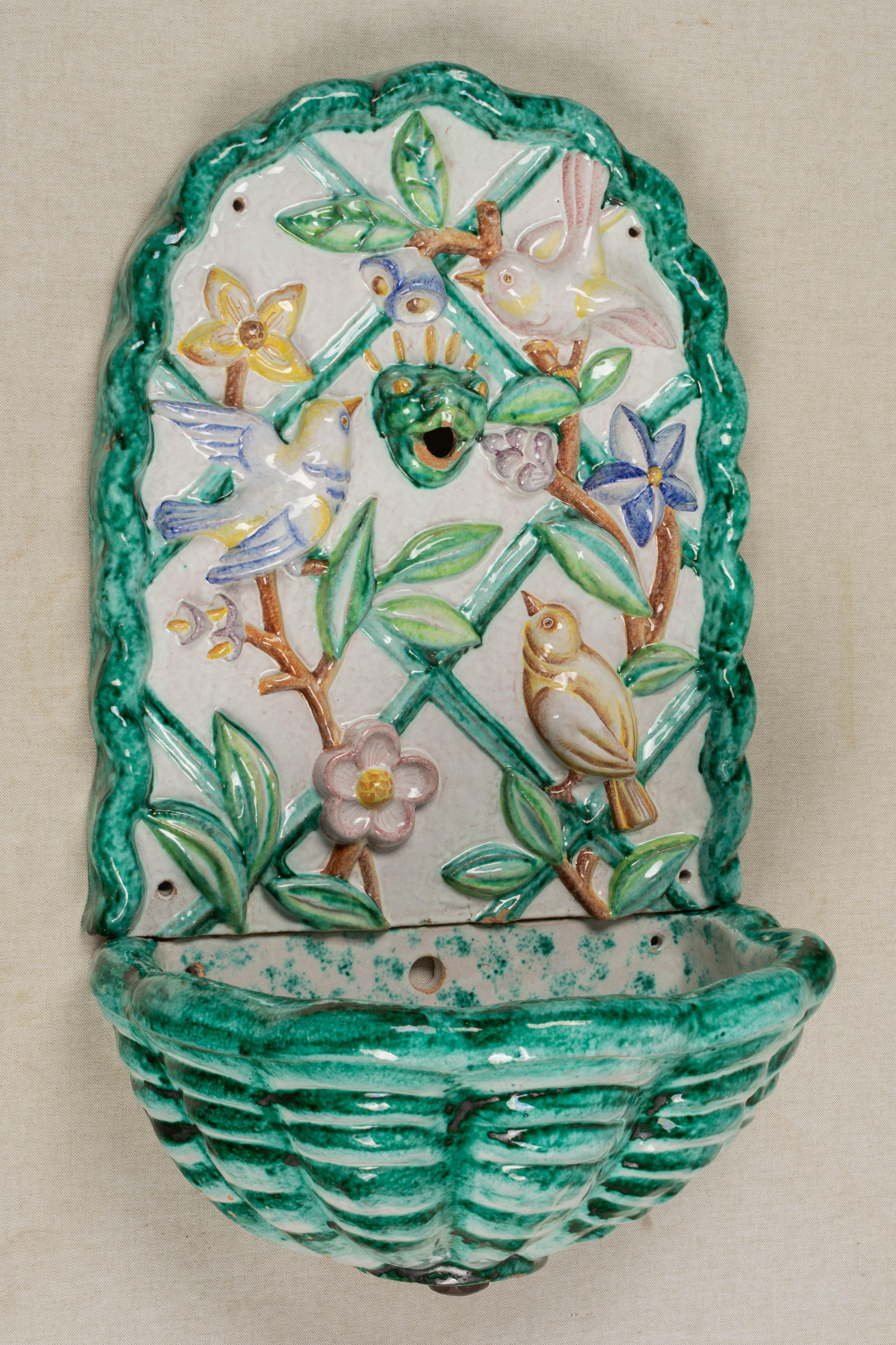 A midcentury Italian glazed terracotta wall fountain, or lavabo. In two parts with a decorative plaque above a demilune basin. Fountain back has an Art Deco style relief of birds and flowers on a trellis with whimsical frog head spout in the center.