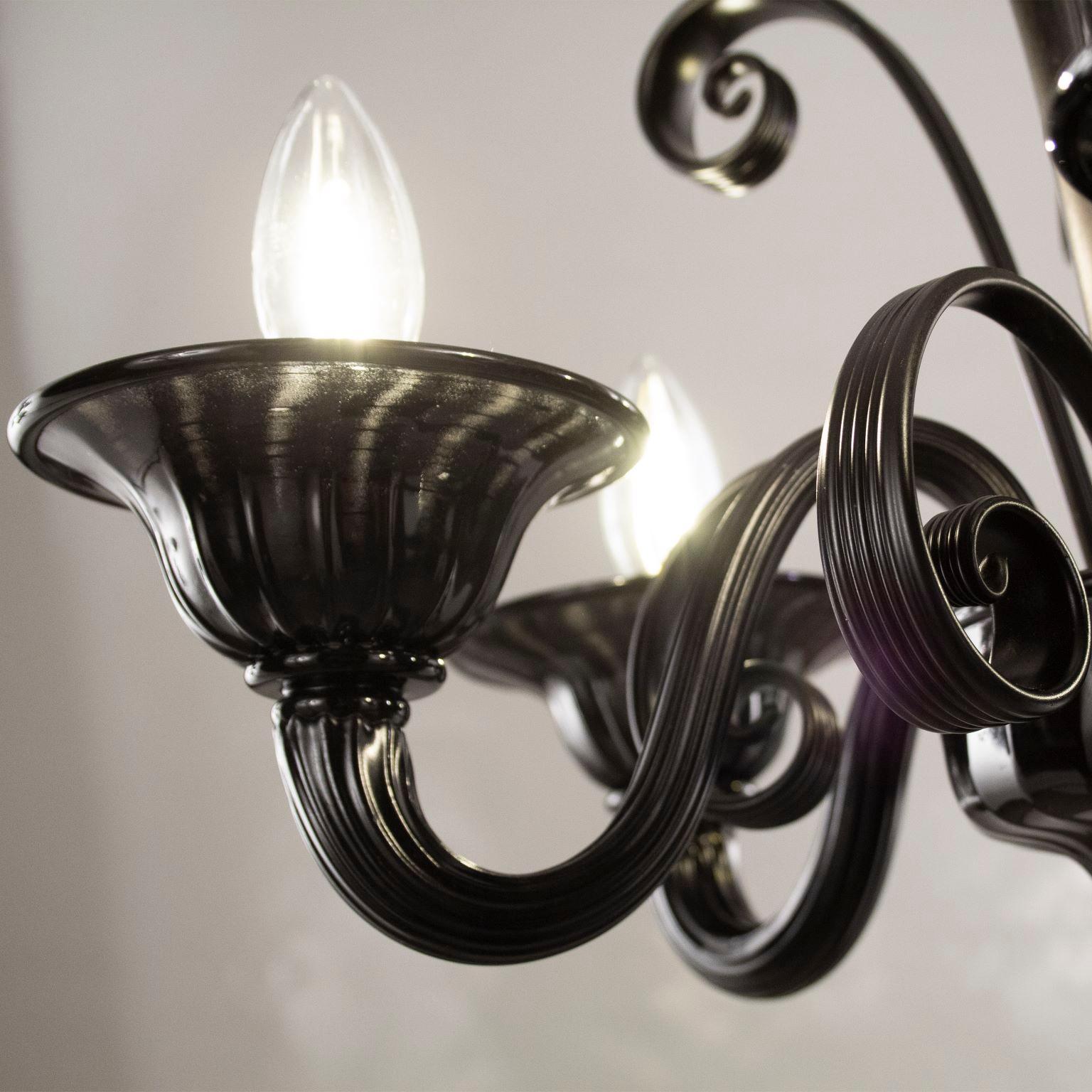 Capriccio by Multiforme is a chandelier, in black artistic glass, with curly ornamental elements.
Inspired by the classic Venetian tradition it is characterized by a central column where many blown glass “pastoral” elements are installed. These curl