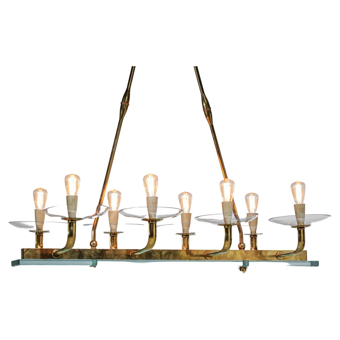 Italian chandelier from the 60's in the style of the work of. Solid brass structure, glass crossbar and cups, lacquered metal socket covers (original paint). Note the nice details of the work on the glass bar fasteners and the end of the brass