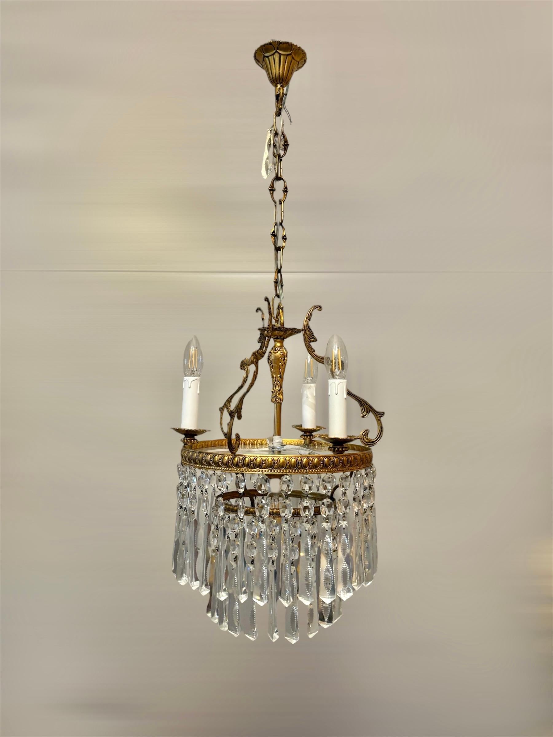 Elegant Italian chandelier from the 1950s, featuring a finely crafted gilded brass structure adorned with sparkling Bohemian crystals. The chandelier is designed with 4 lights, 3 styled with candle-like holders, and a central light enhancing its