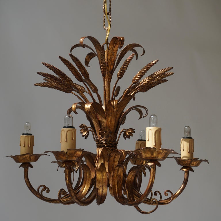 A Hollywood Regency six-arm light fixture from Italy manufactured in midcentury (1960s-1970s). It is in the form of a bunch of wheat sheafs and it is made of antique leaf gold plated metal. The lamp has six sockets for small screw base bulbs or LEDs