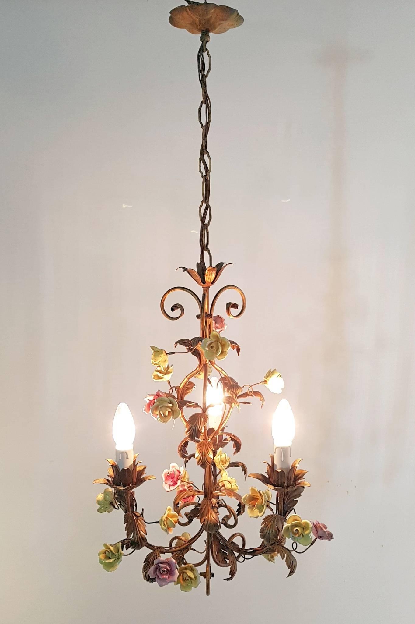 A charming Italian painted tole three-light chandelier with yellow and pink porcelain flowers in good condition but with some chips to some of them. This chandelier retains the original sockets and has not been rewired but is working well. The
