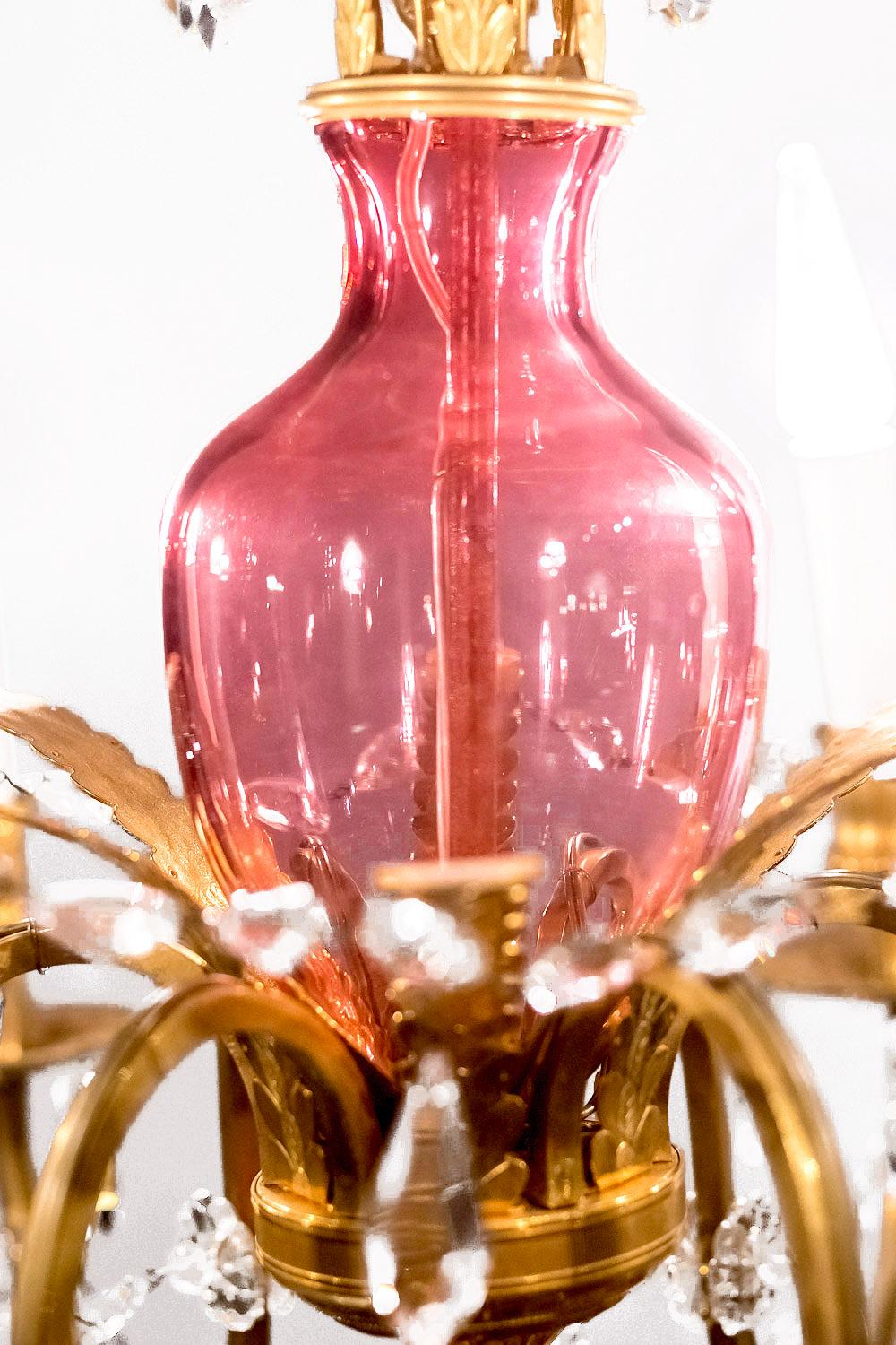 Chandelier in gilt bronze and pink and transparent glass. Model with a crown composed of gilt bronze pending rods supporting transparent glass drop tassels.
Central shaft composed of three pink glass balusters centred by a gilt brass stick. Decor of