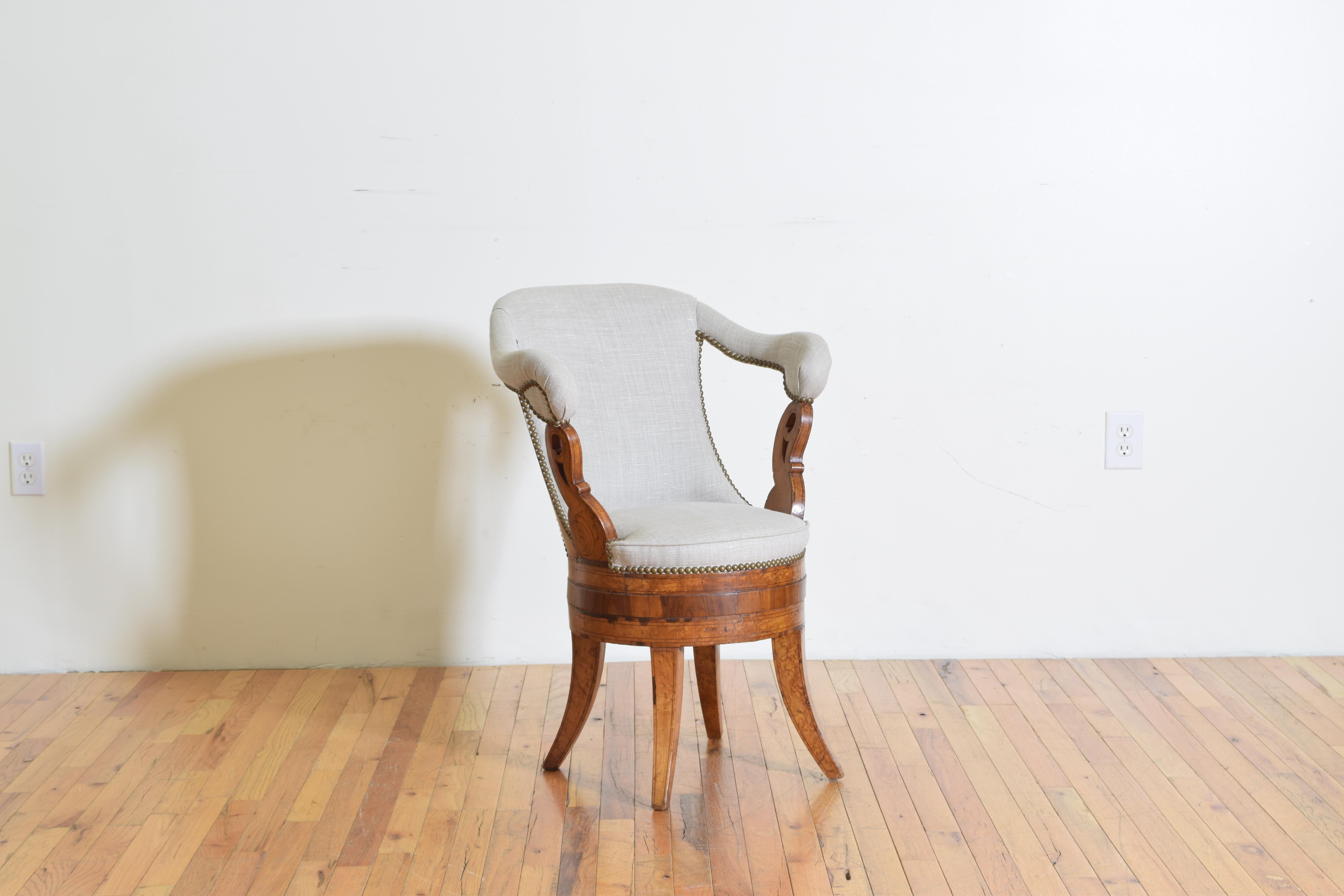 This unusual chair has a sloping back with high, upholstered arms and is a slightly later rendition of an Empire period chair, constructed of maple and rosewood veneers, raised on splayed legs the arms are atop almost swan-like shaped supports,
