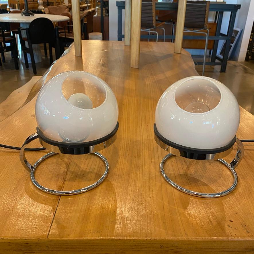 Italian Mid-Century Modern table lamps by Fabio Lenci for Guzzini, c. 1960, white opalescent art glass shades in an adjustable chromed metal stand. Eye-ball shaped pair, predecessors to the post-modern style.