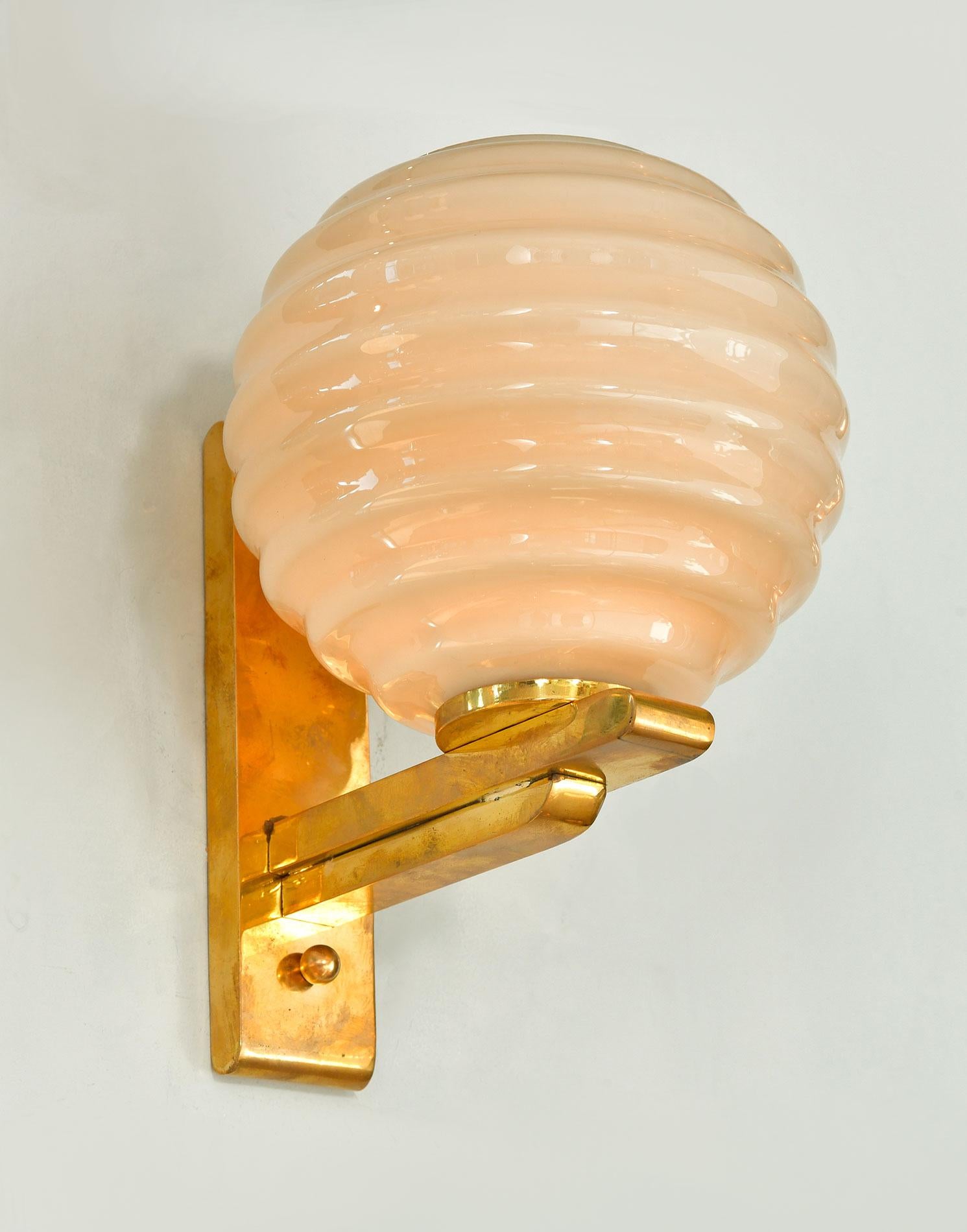 Chic wall lights each with a brass bracket holding a ribbed cup of cream glass. Exudes a lovely warm light.