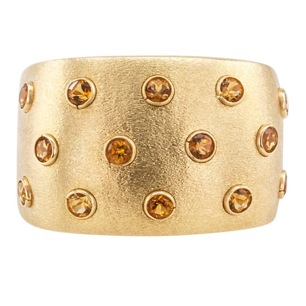 Italian citrine and gold ring band circa 1980. The wide band is decorated by a rich texture applied to the gold surface and studded on the top, at equal intervals, by fourteen round bezel-set citrines. Crafted in 18-karat yellow gold and stamped
