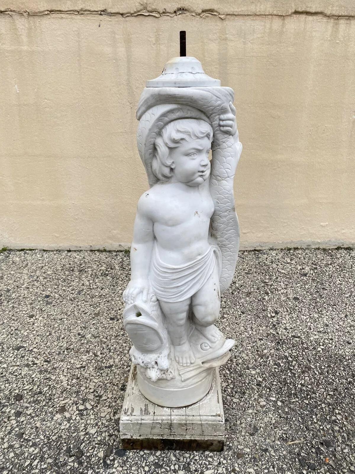 Statue de fontaine de jardin en marbre sculpté de chérubin et dauphin. L'article est caractérisé par un poids d'environ 70 livres. Nous ne savons pas si la fontaine fonctionne. La statue de marbre est montée sur un socle en bois et il n'y a pas de