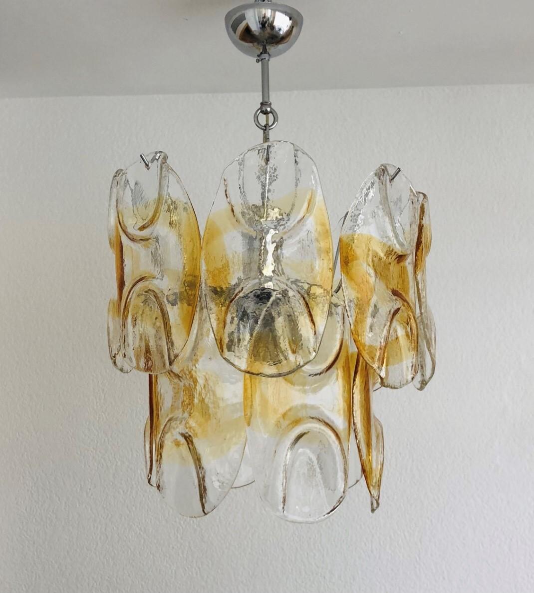 Stunning Italian amber clear Murano glass midcentury chandelier. This chandelier was designed and manufactured during the 1960s in Venice (Italy) for the company “AV Mazzega”. 
The chandelier is equipped with three light sockets (E14). A