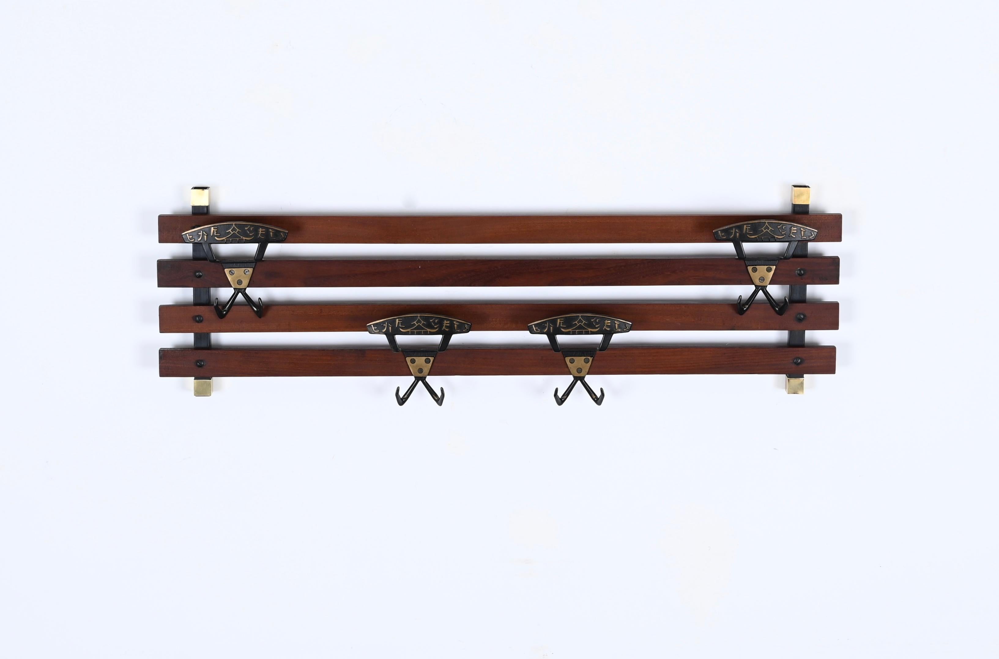 Gorgeous coat rack in teak wood, brass and enameled metal. This lovely piece was realized in Italy in the 1960s.

This elegant coat rack has two black enameled iron supports with brass accents connected by four solid teak wood bands. The sturdy