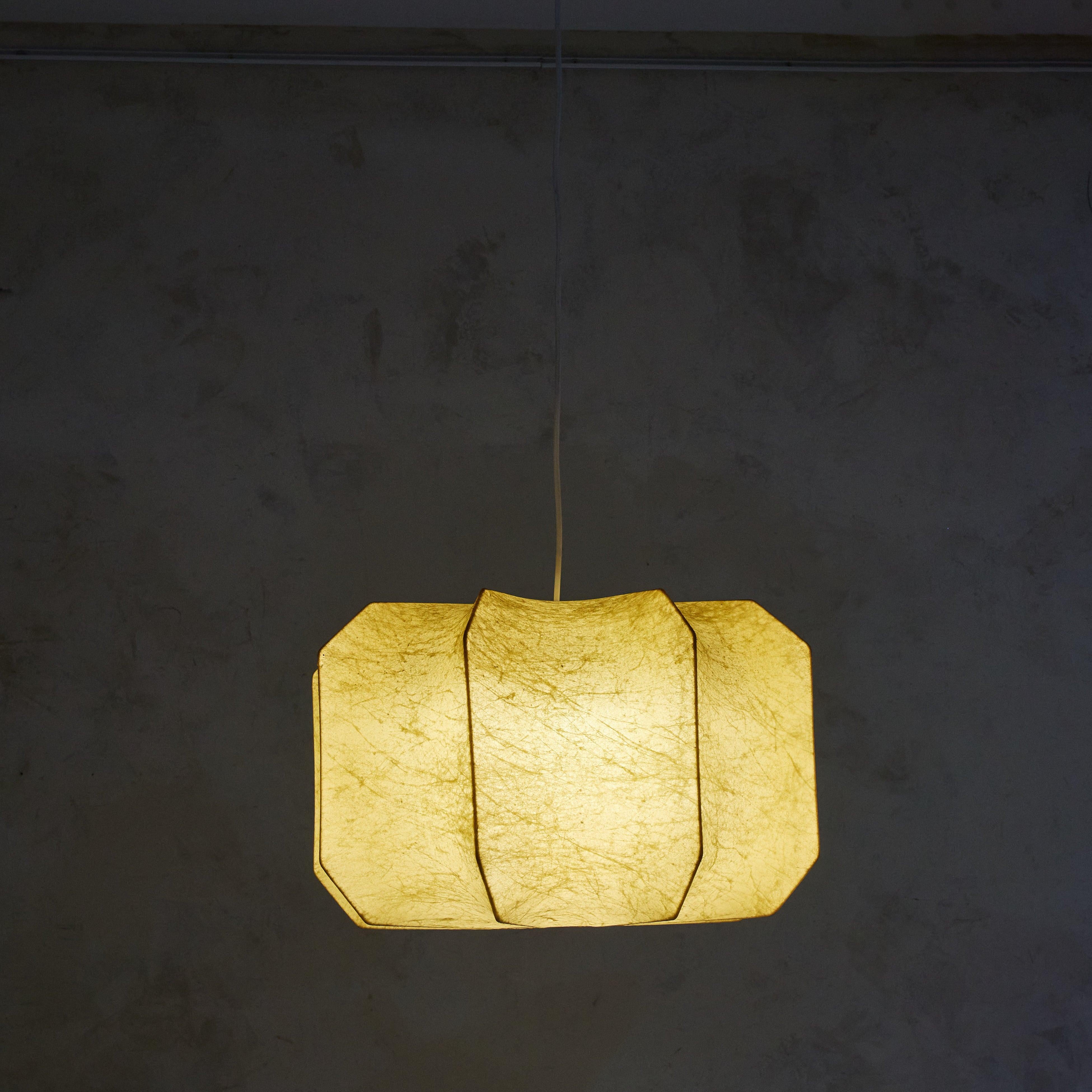 A 1960s Italian cocoon pendant featuring a metal frame and a 'cocoon' sprayed resin shade, mimicking the look of goatskin parchment. This pendant has an angular barrel shape with curved channels and includes a new white canopy. When lit, it emanates