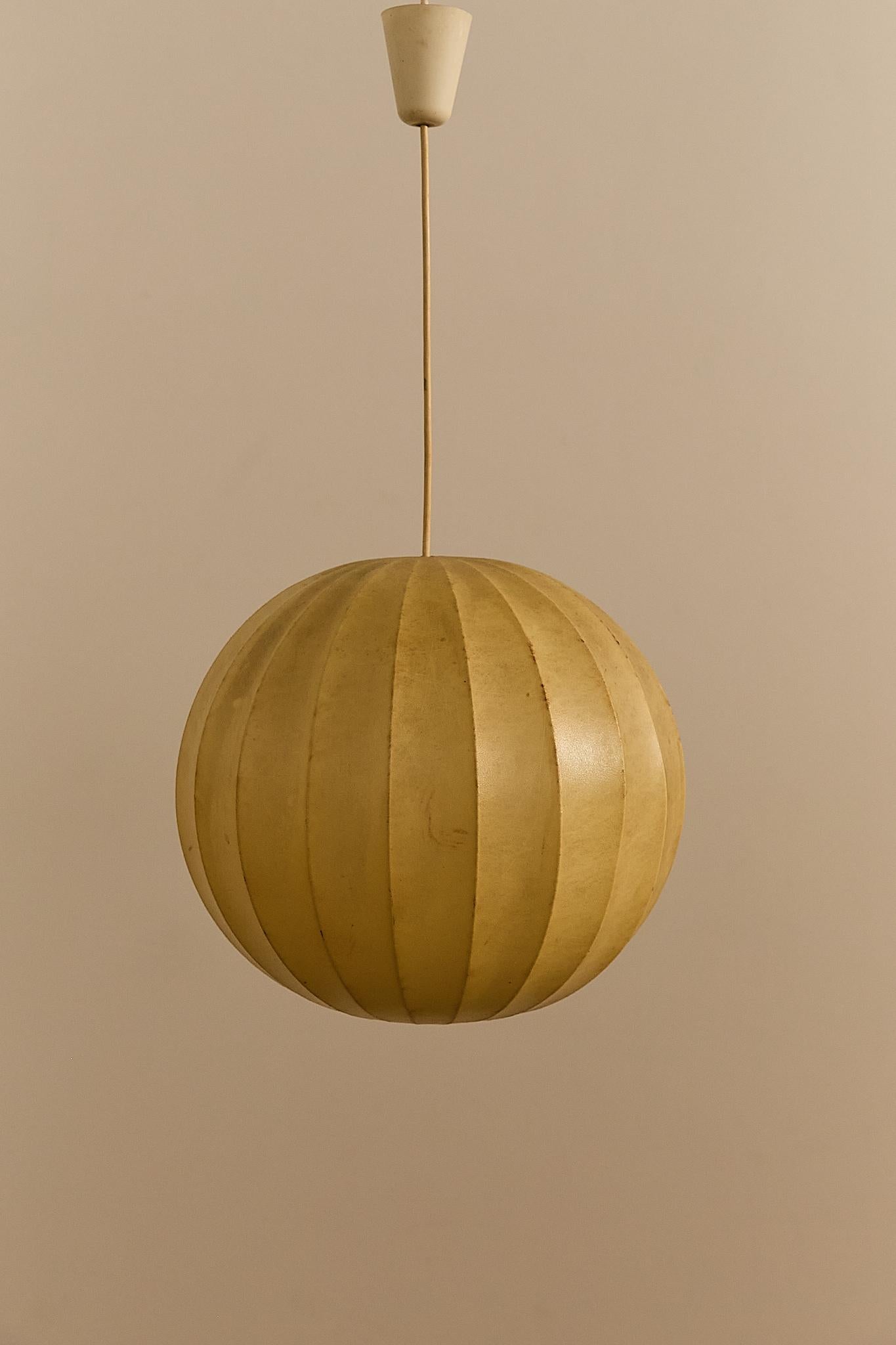 Una scultorea lampada a sospensione italiana degli anni '60, realizzata con la tipica tecnica del bozzolo. Il paralume sferico è formato da una resina polimerica spruzzata su una struttura metallica, che crea una luce calda e diffusa quando viene