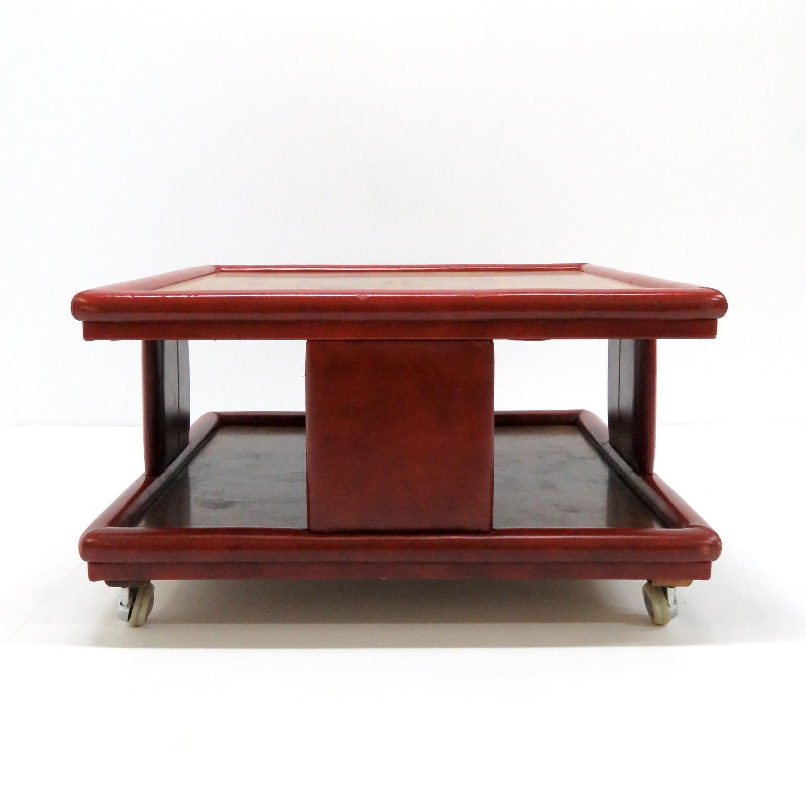 Wonderful red leather and wood two-tier coffee table from Italy, 1970, attributed to Poltrona Frau. One dark and one light wood top, wrapped in ox-blood colored, patinaed leather, on detachable casters.
  