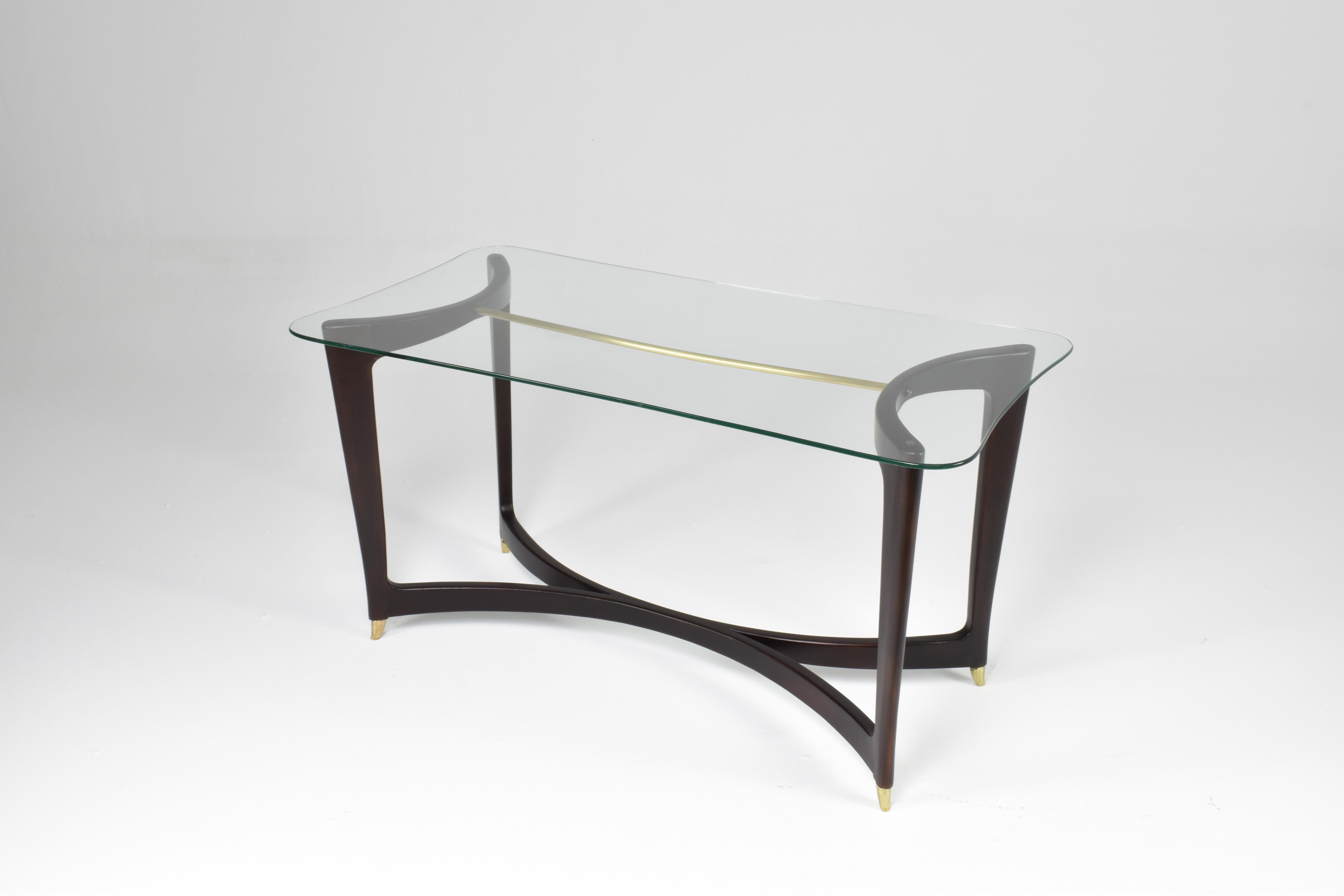 A beautiful Italian 1950s coffee table with elegant curves, a beautiful glass tabletop highlighted by a brass detail that crosses the sophisticated structure. 
Meticulously restored at our atelier. 
In Guglielmo Ulrich