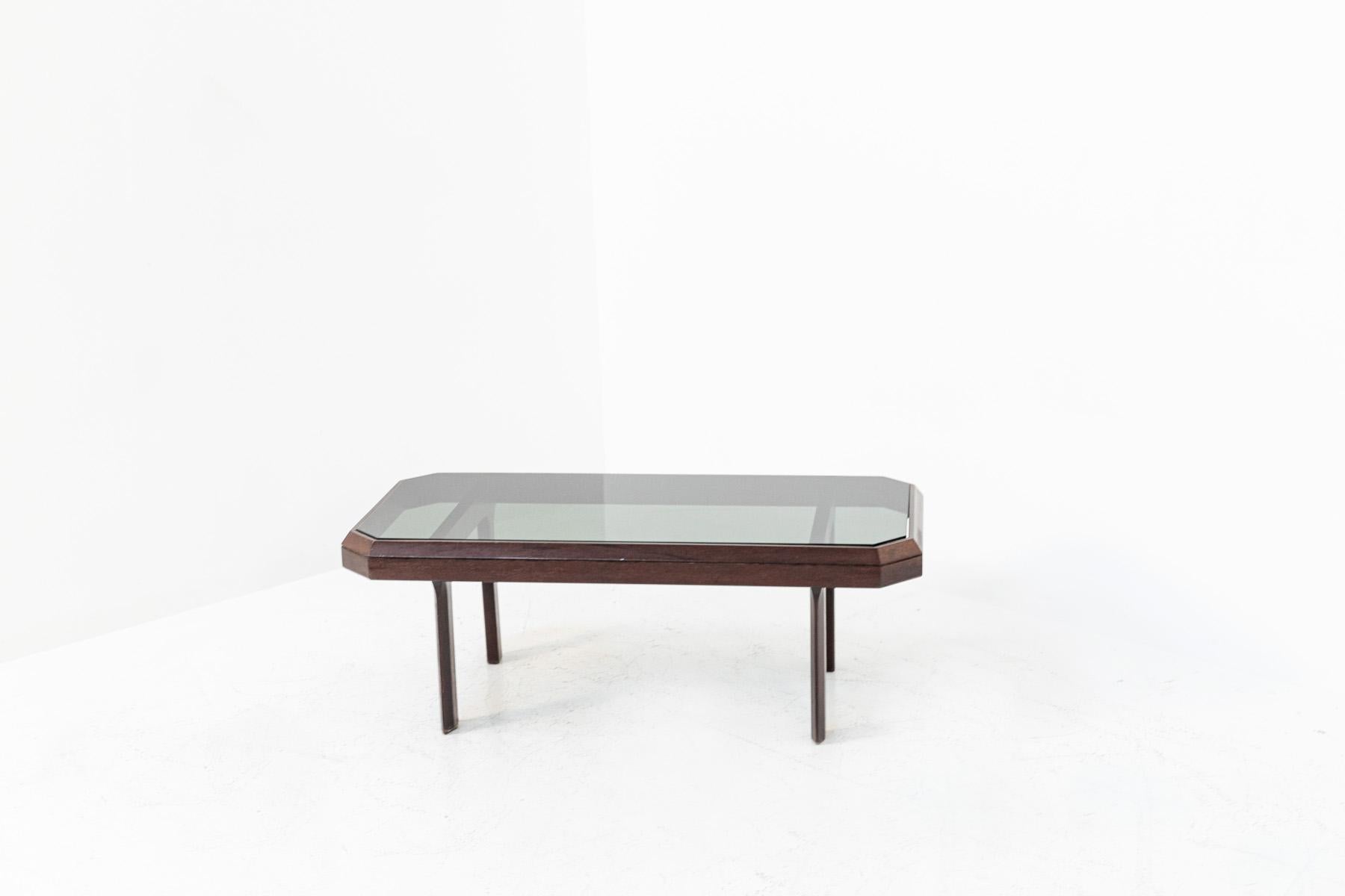 Italian coffee table from the 70's in dark walnut wood. The coffee table features beautiful clean lines. Its table top has right angles in a hexagonal shape. Its table top is made of smoked glass also in hexagonal shape. Its legs are also in line