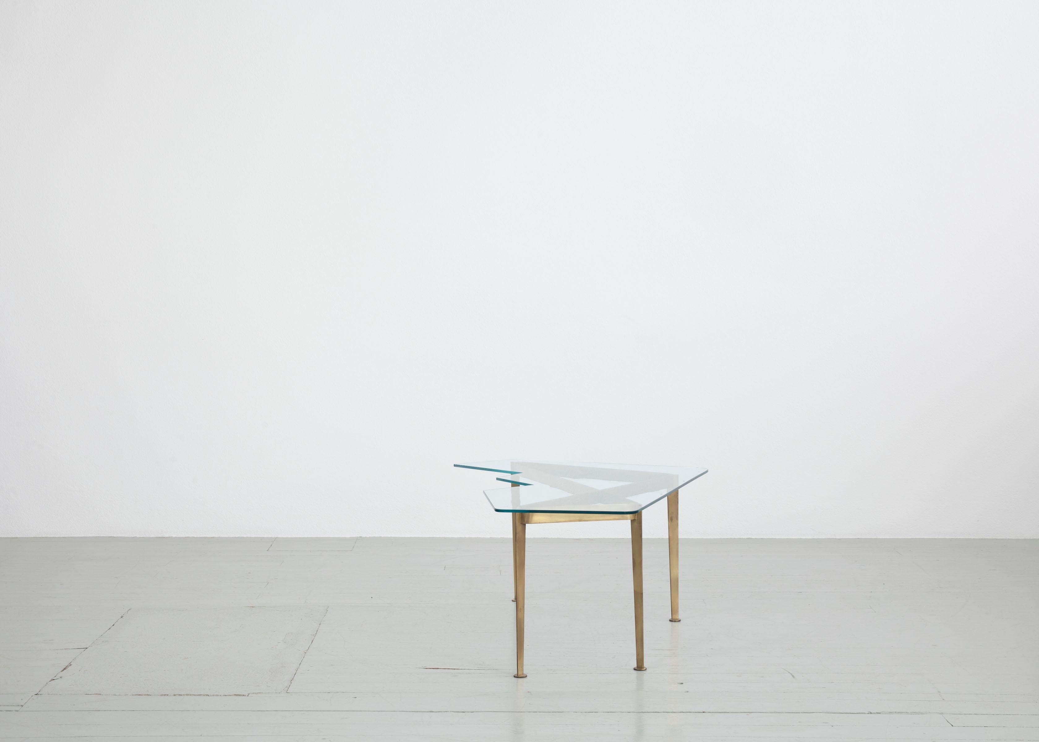 Cette table de canapé asymétrique a été fabriquée en Italie dans les années 1950. Le plateau en verre de cristal taillé est soutenu par un cadre en laiton, qui sert également d'élément décoratif. Le plateau de la table est en très bon état