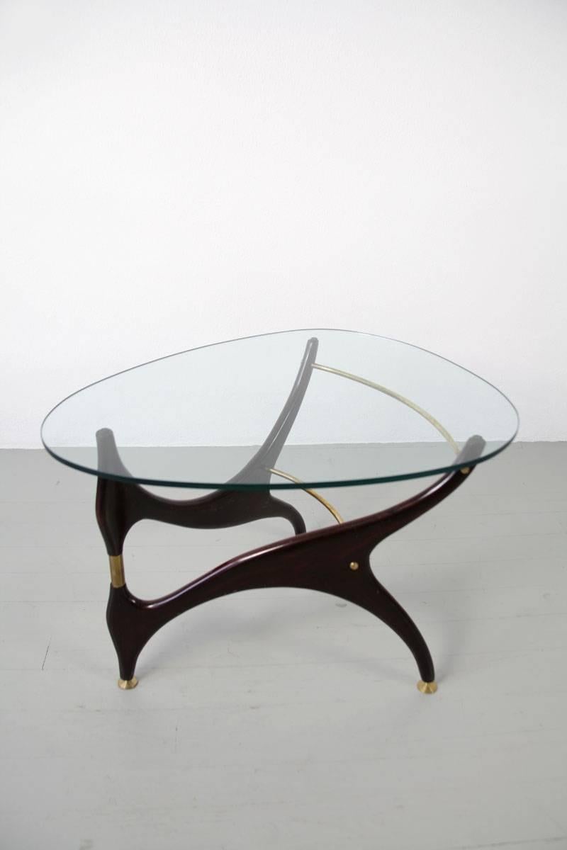 Side or couch table, Italy, 1950s. The table is made out of dark painted birchwood and reminds of designs by Carlo Mollino. The egg-shaped glass top unifies the organic forms. The brass elements become decorative and necessary structural element for