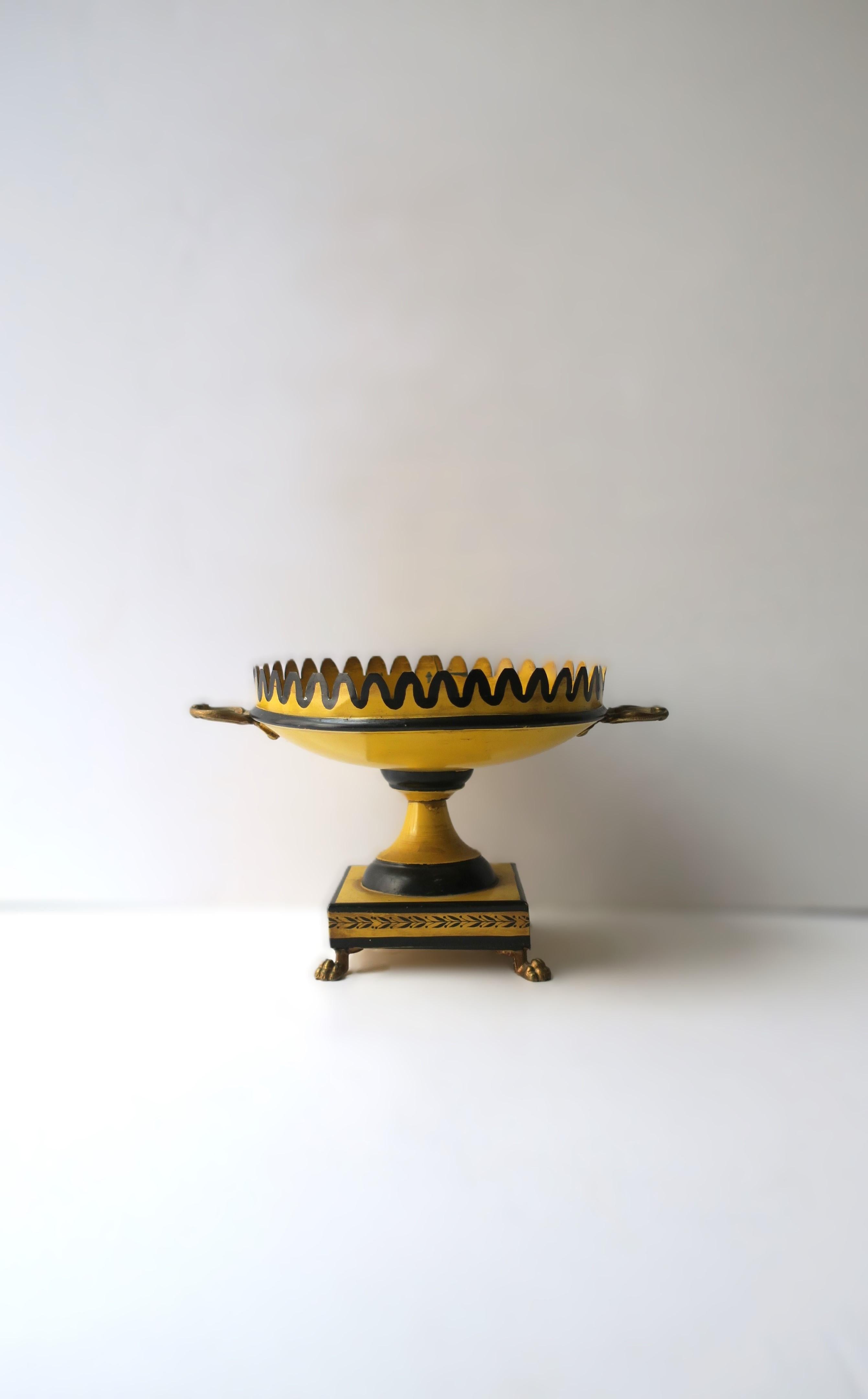 A beautiful Italian tôle footed compote tazza with scalloped edge and lion paw feet, in the Regency Style, circa early to mid-20th century, Italy. Piece is a rich yellow with black detail (scalloped edge, Regency scene center, decorative base),