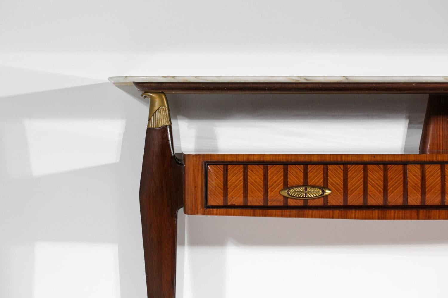 Elegant Italian console from the 1960s in the style of the work of Paolo Buffa. Solid wood and veneer structure with a nice marquetry work on the three drawers. Marble top supported by feet overhung by stylized eagle heads. Handles and base in solid
