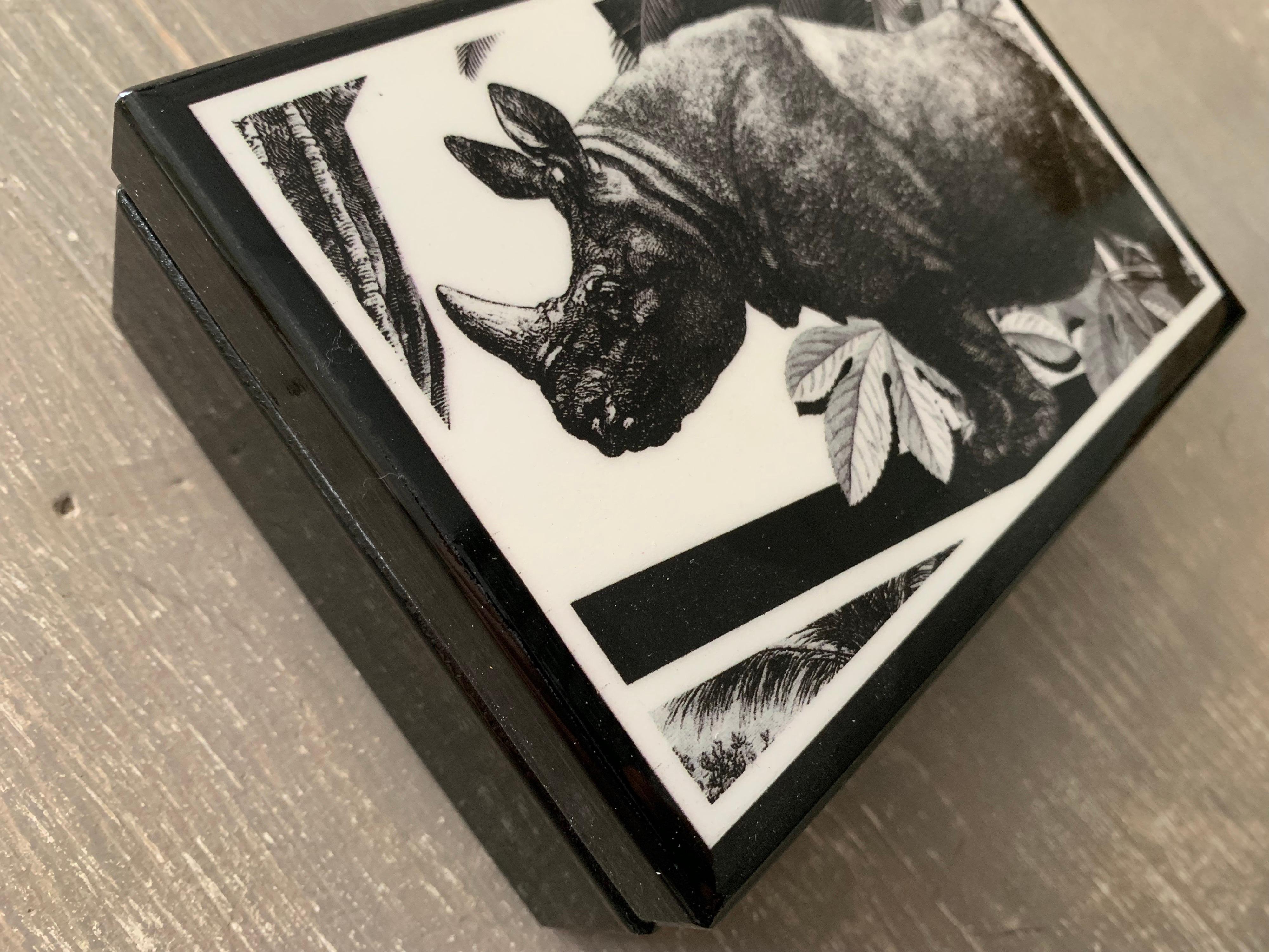 Elegant printed wood box portraying an exotic natural setting with a rhino on it. 

This object is part of a large collection called 