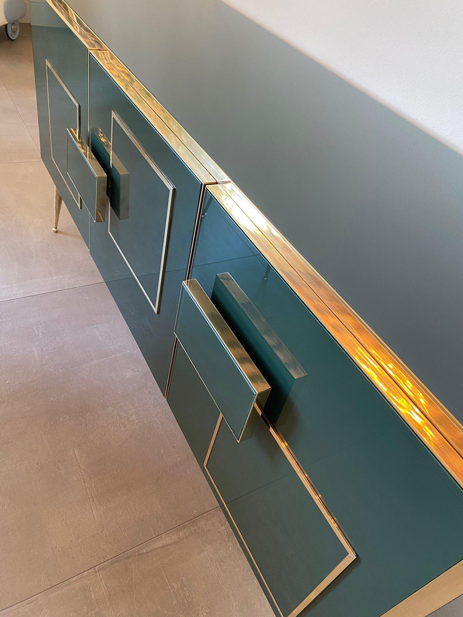 Beautiful sideboard designed and handcrafted by us with structure and interior in solid wood, legs and finishes in brass and tops and decorations in emerald colored Murano glass. 
It is an object of high quality and refinement, ideal for giving