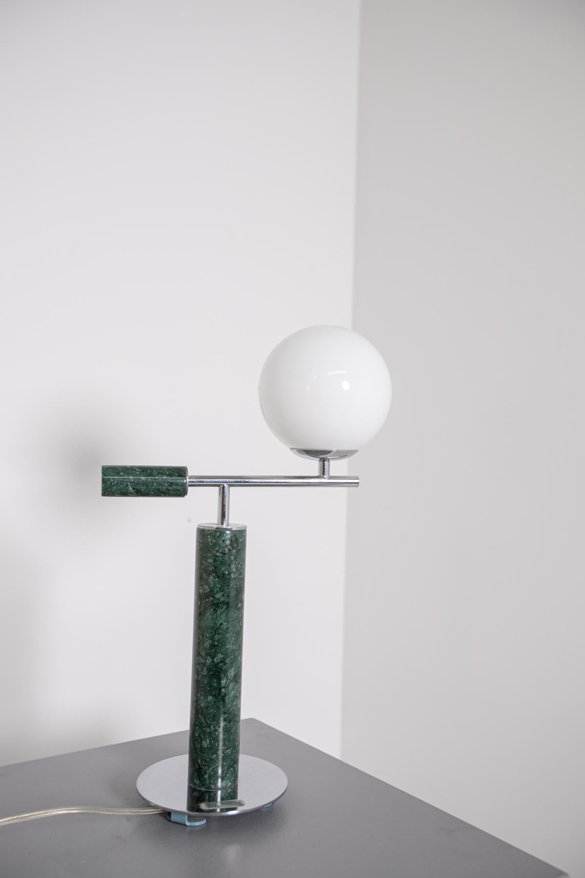 Contemporary table lamp from 2019 Italian production. The table lamp through its sculptural shapes create a geometric play to the object. Made with a central body in alps green marble with steel base , the peculiarity of the lamp is its steel arm