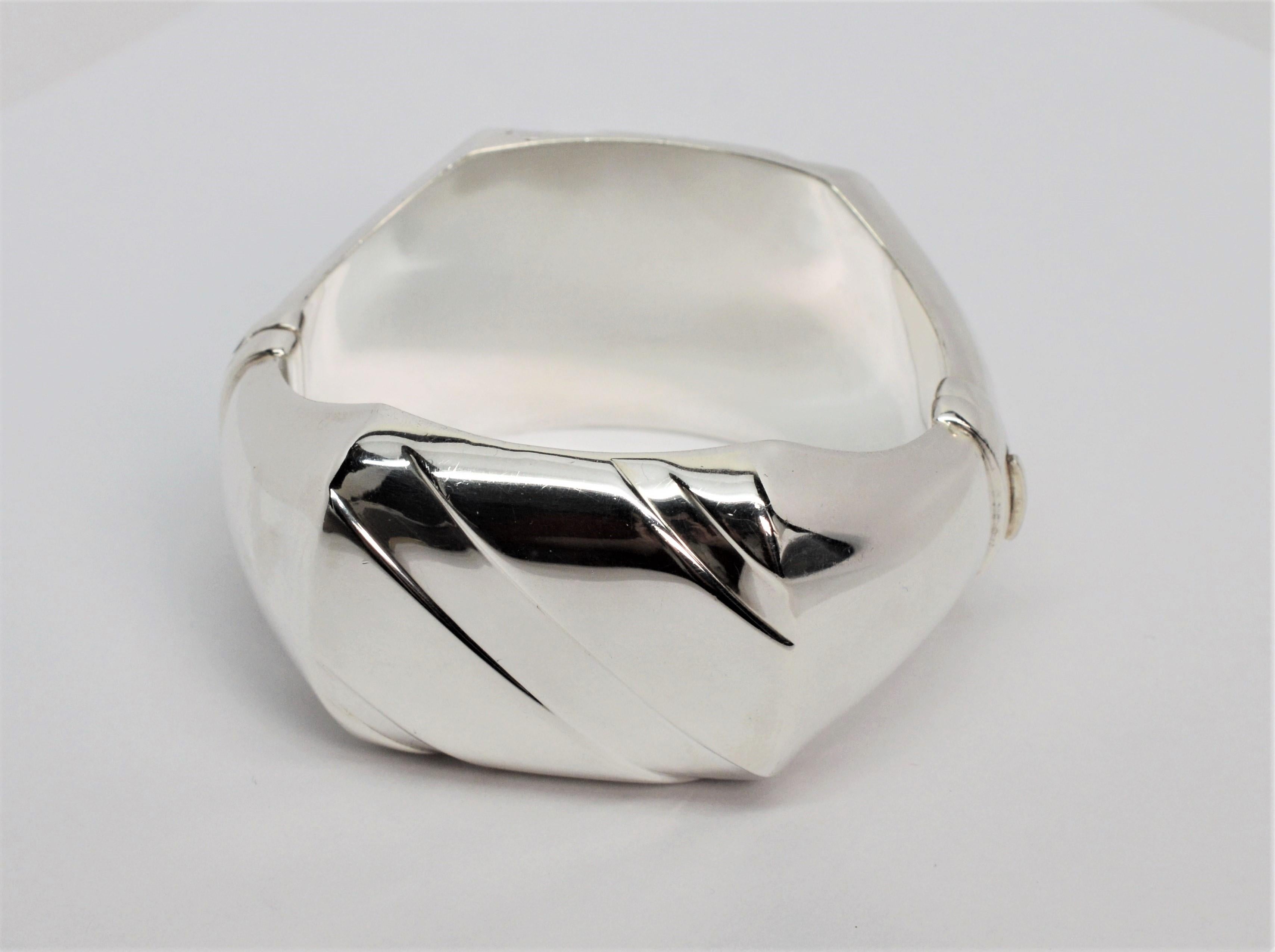 Contoured in sterling silver with a high luster, mirror like finish, this wide bangle has a bold contemporary look. The piece flows around the wrist graduating to feature plackets, front and back, enhanced with asymmetrical lines. All constructed in