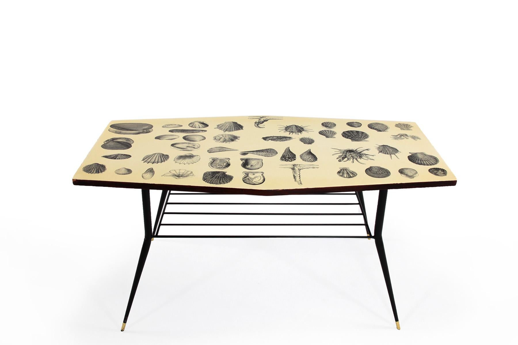 This side table was designed in Italy in the 1950s. The table frame is made of black lacquered iron with brass ends and has a small shelf under the table top. The table top is decorated with a shell motif reminiscent of designs by Piero Fornasetti