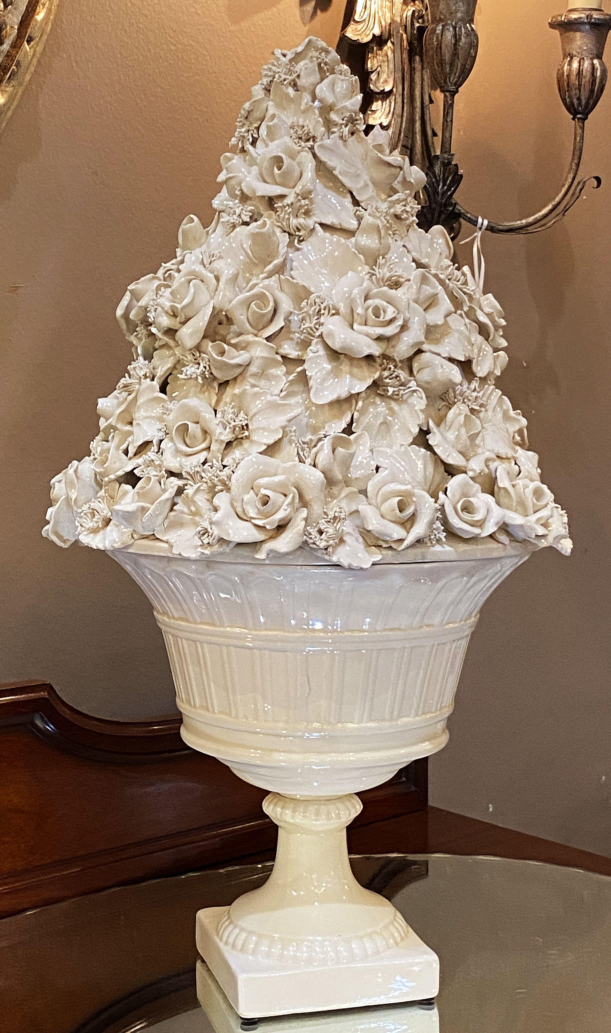 Gran cuenco italiano de pedestal, de cerámica esmaltada blanca o crema, con tapa en relieve de rosas (o rosetas) y bocage en toda la circunferencia, sobre un cuerpo inferior con cuenco y soporte de pedestal sobre una base de plinto cuadrada.

Ideal